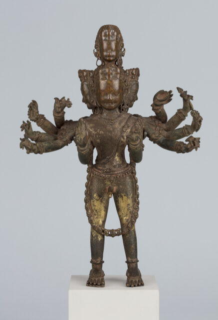 Tarnished copper sculpture depicting many-armed and -headed deity standing with feet planted firmly apart