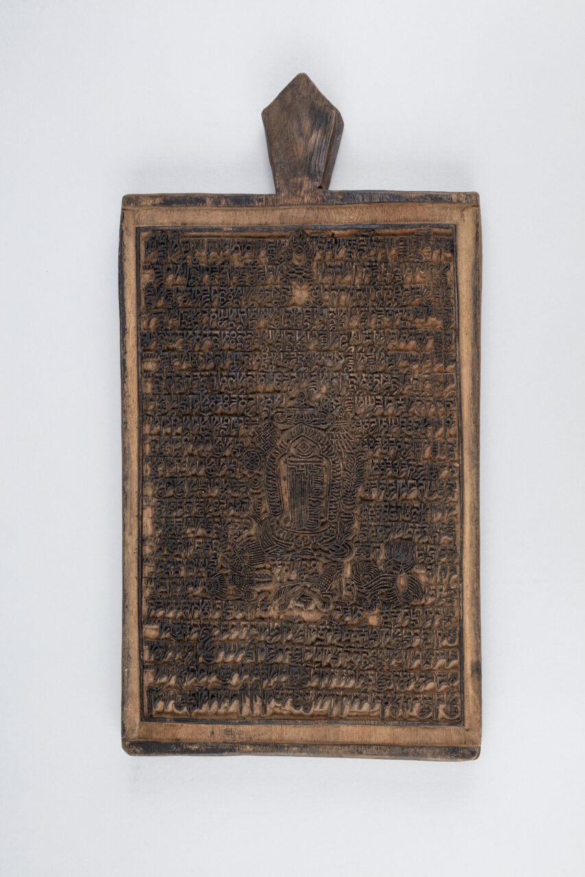 Rectangular ink-stained woodblock incised with dense text and image; lozenge-shaped handle at top