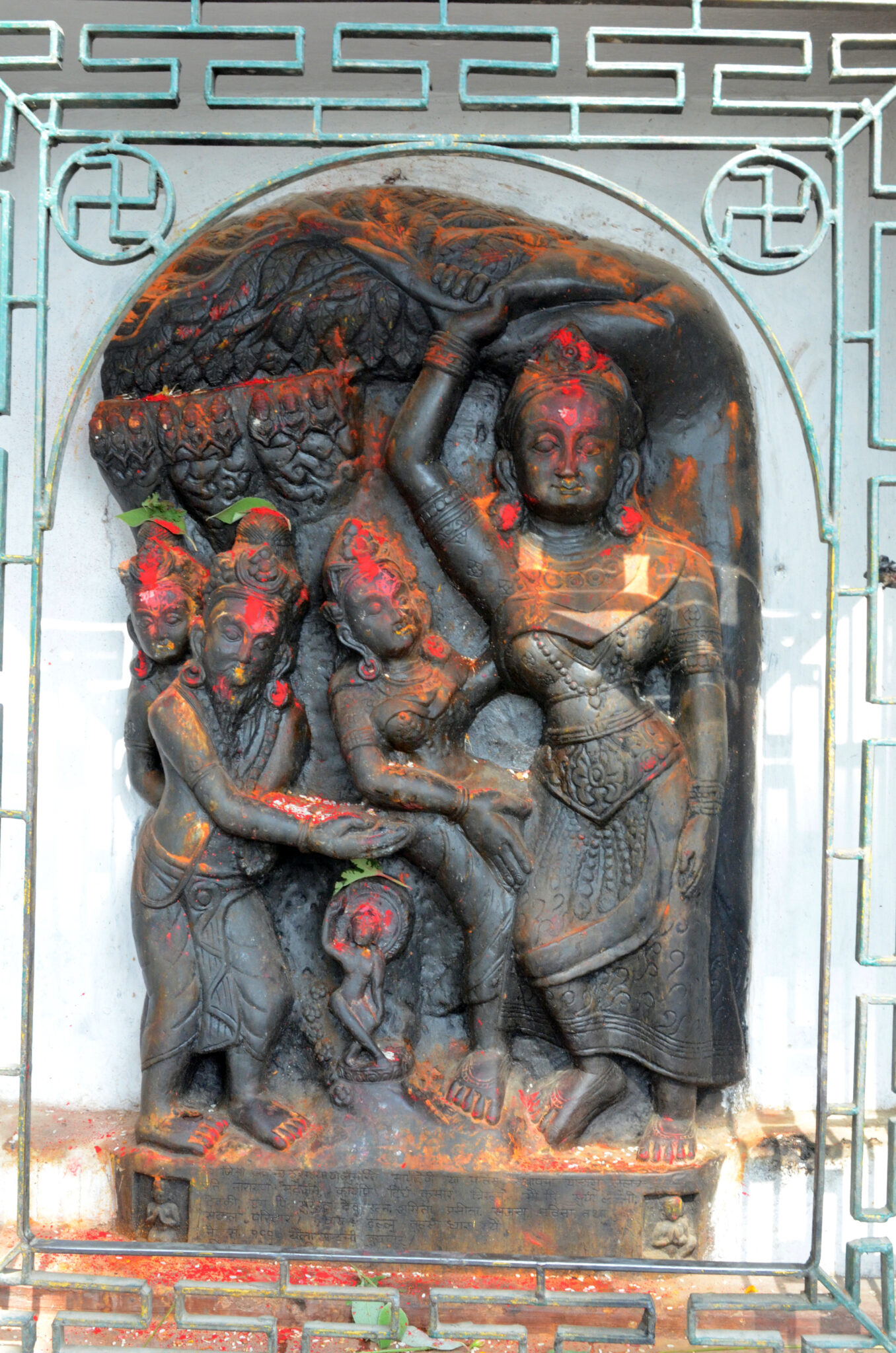 Stone relief daubed with pigment of woman attended by three figures; housed in niche behind open grille