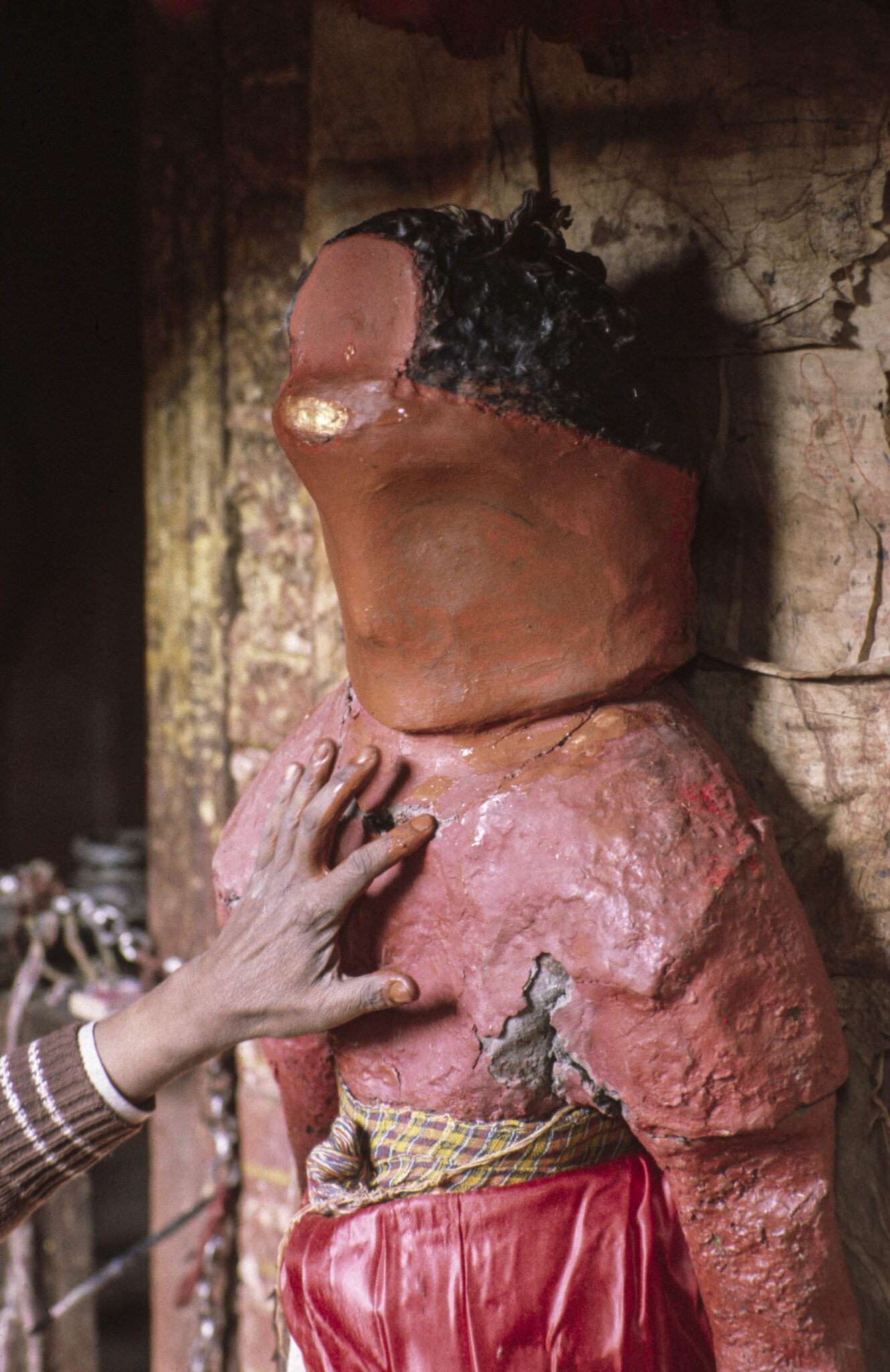 Hand of a restorer applies material to damaged red and ocher statue