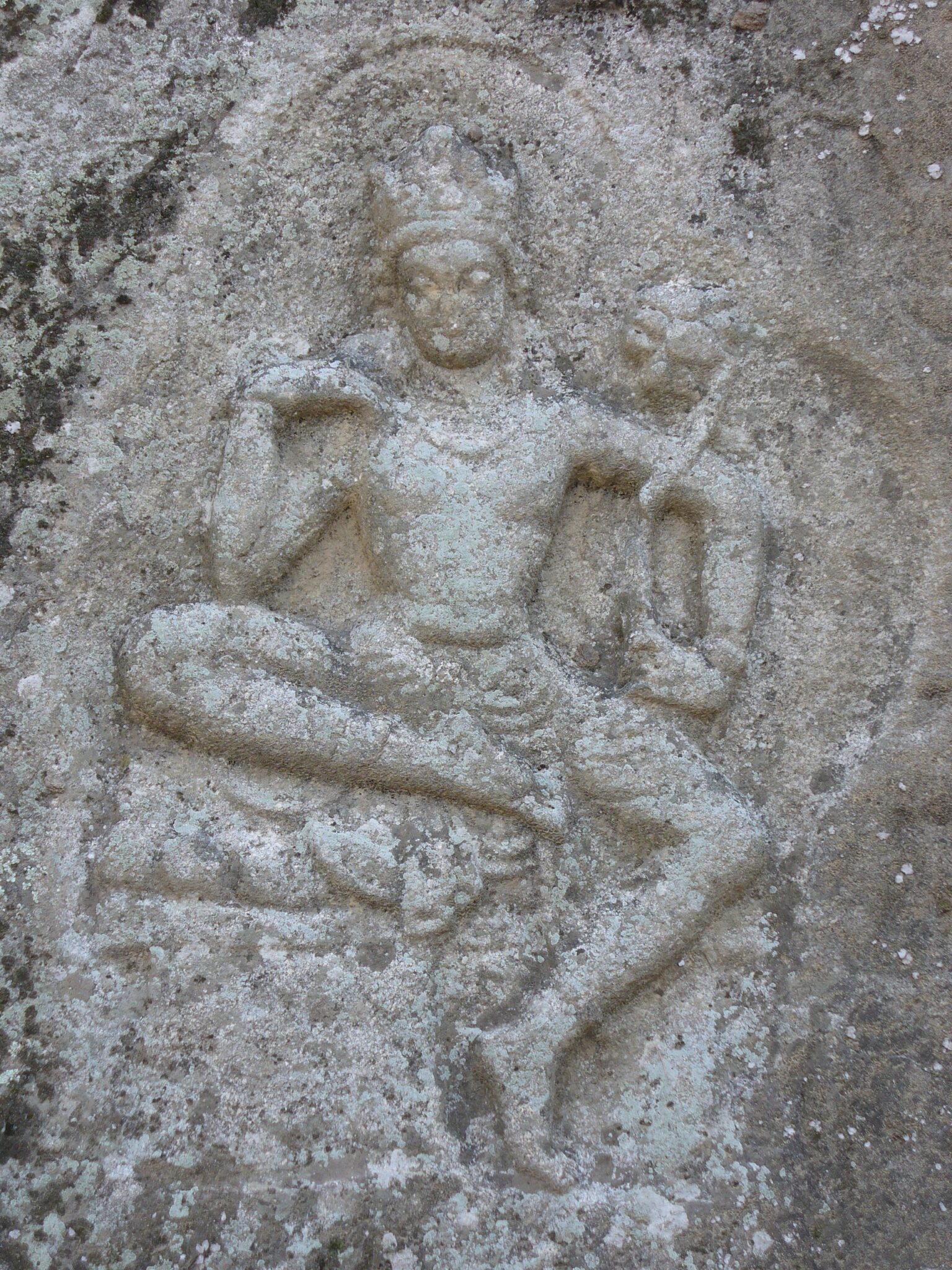 Weathered relief in grey stone of seated Bodhisattva with arms bent and one foot touching ground