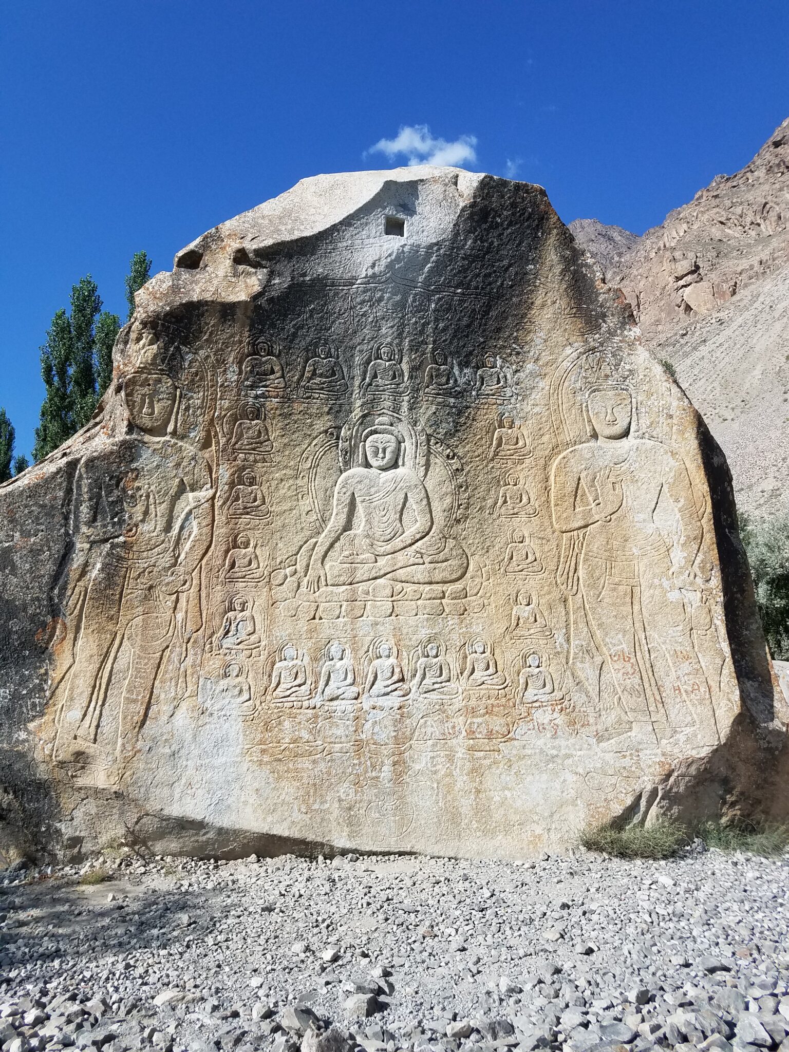 Seated Buddha enclosed in frame of 20 smaller buddhas and flanked by standing bodhisattvas; carved into weathered boulder