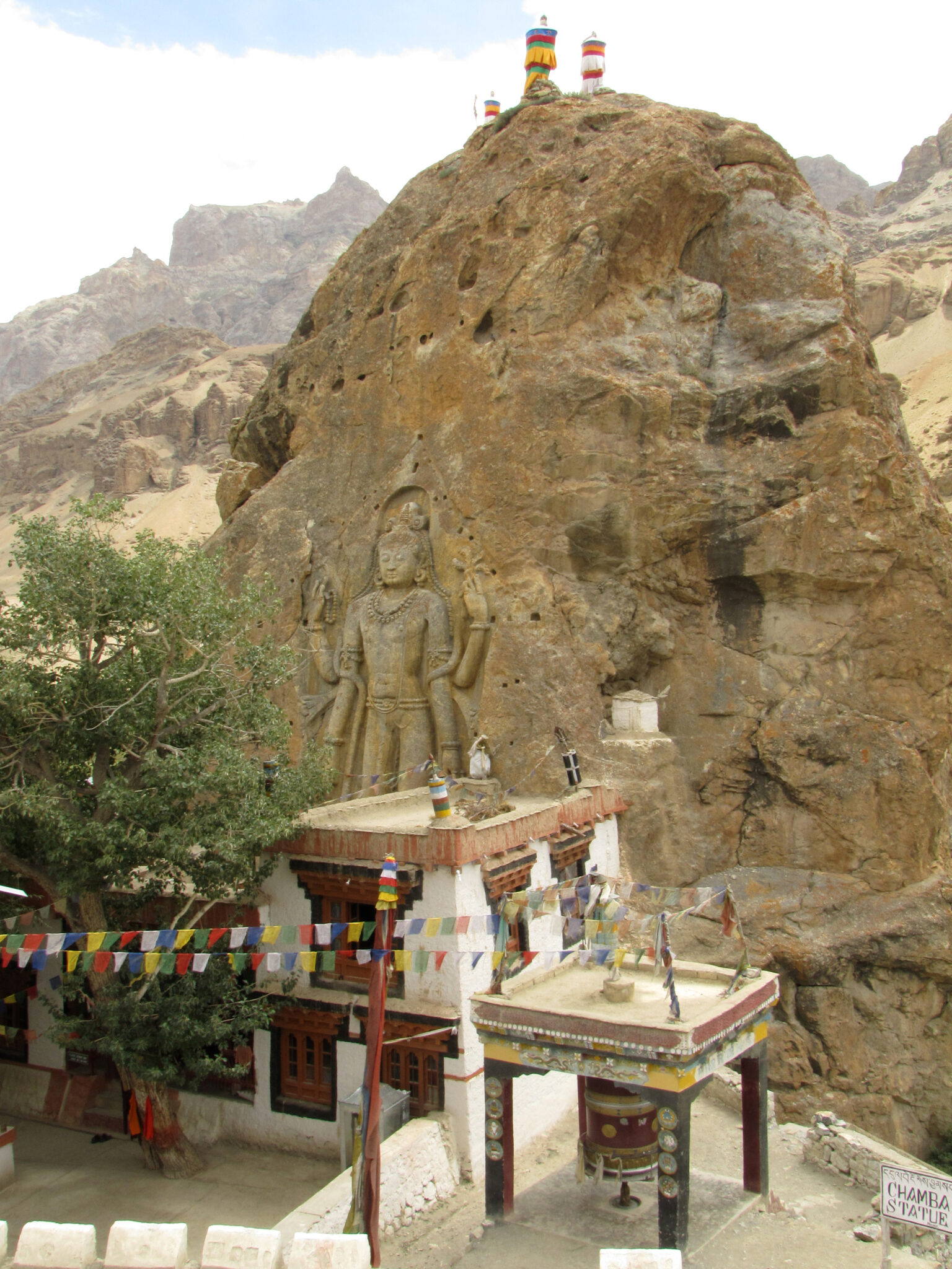 Monumental standing Buddha carved onto face of rock formation towering behind two-story building