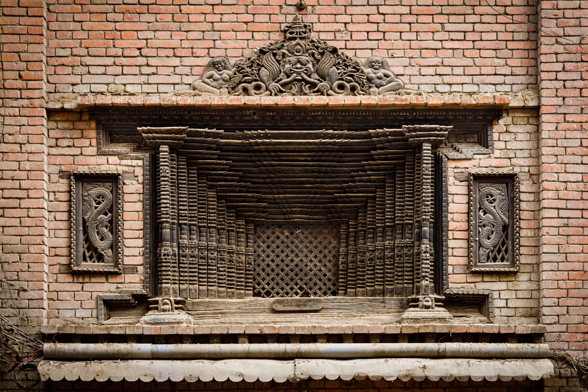 Close view of screened window featuring forced-perspective frame and densely carved semicircular pediment