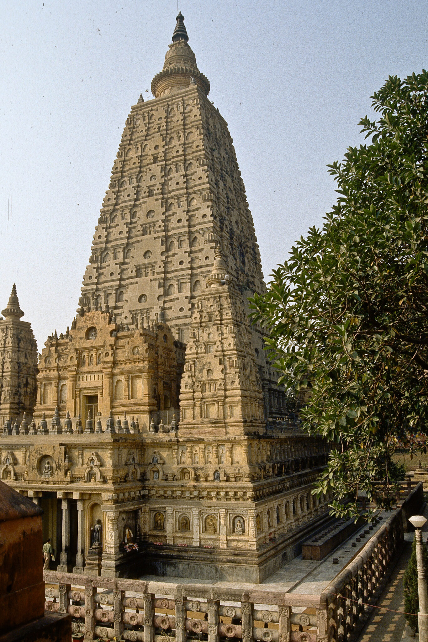 Light yellow tapered tower topped with stupa and covered in geometric moldings; features extravagantly decorated portico and base