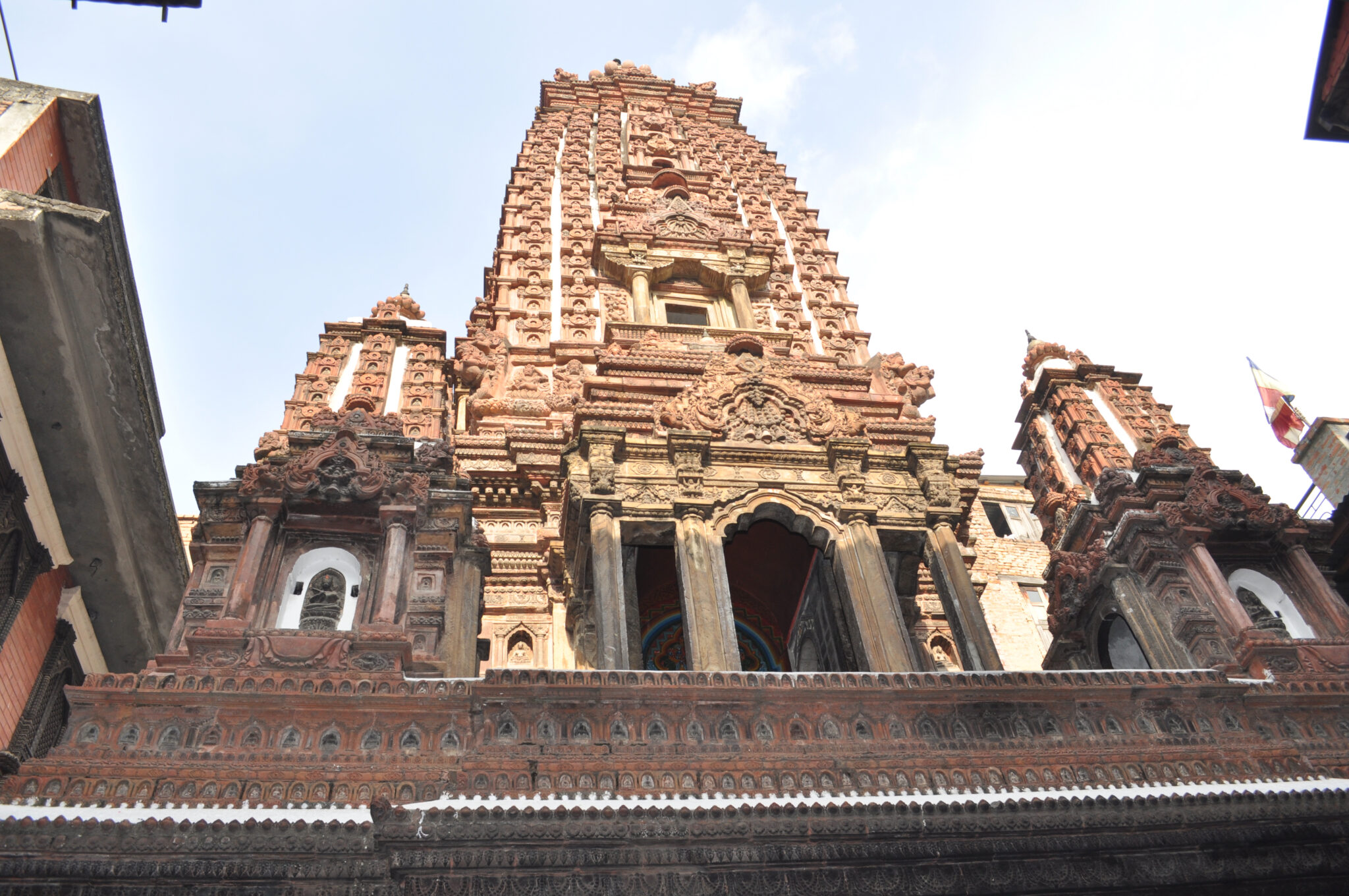 Close view from below of tower clad in decorative molding; features richly carved portico, pediments, and lintels