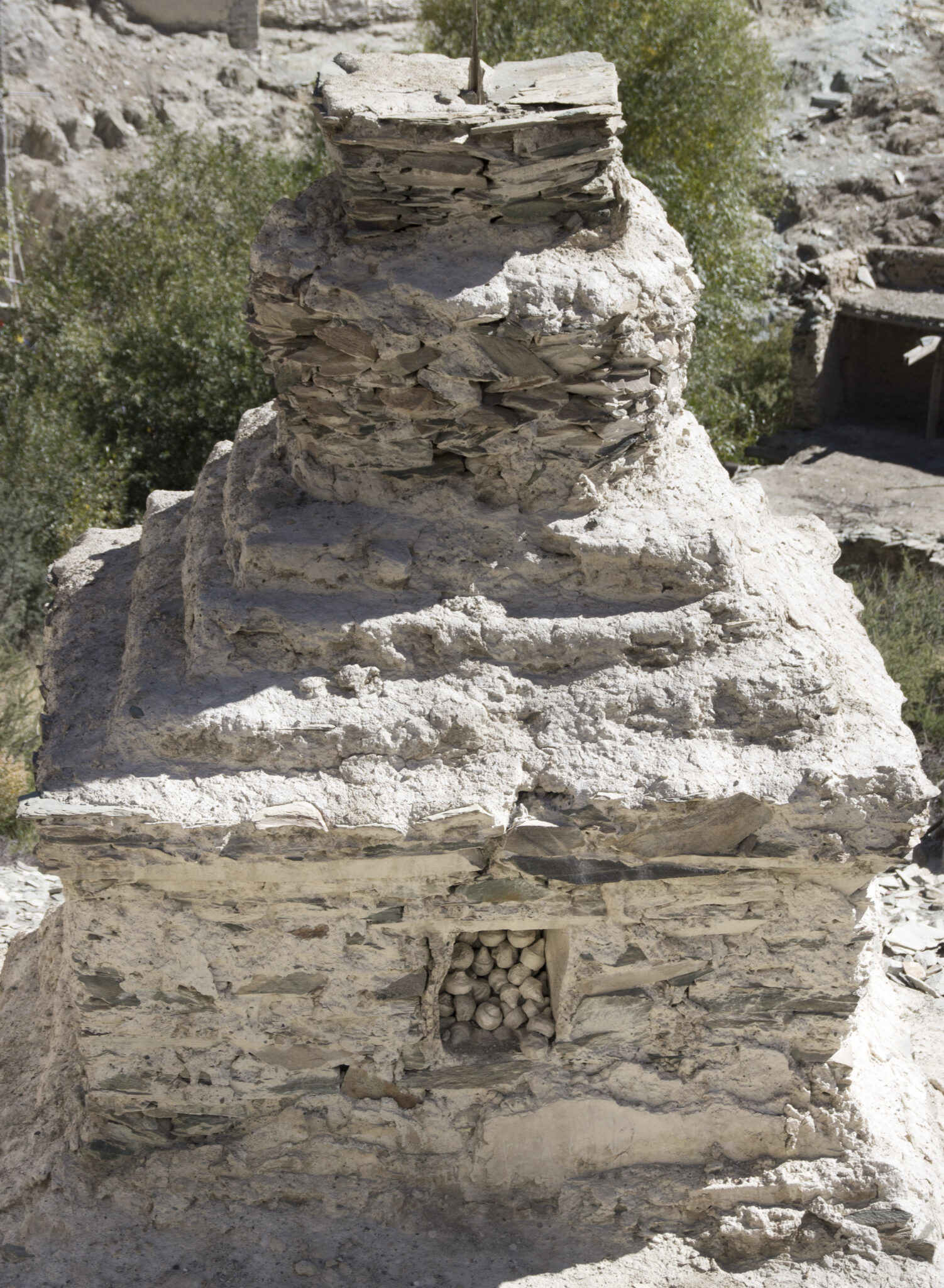 View from above of eroded beige stupa featuring square opening at base filled with round objects