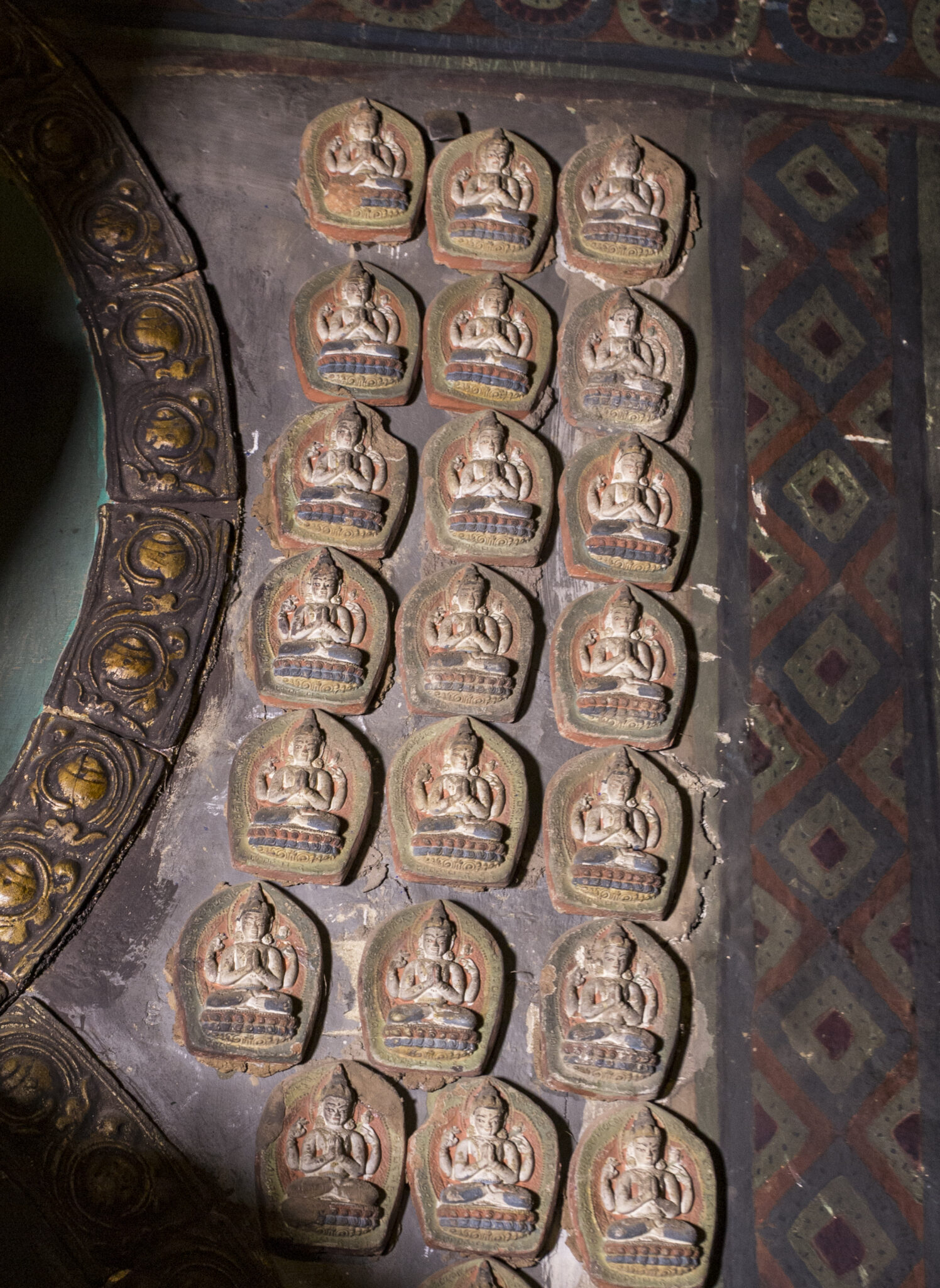 21 brown circular reliefs depicting seated deity arranged on wall in three columns and seven rows