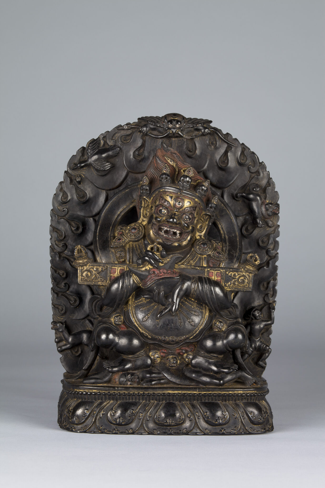 Polished brown stone sculpture with gold and red pigment depicting grimacing deity before nimbus of flames