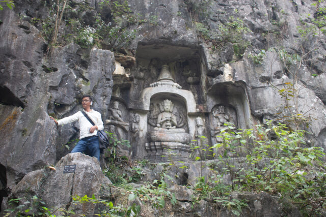 Comprehensive view of niche in rock face containing deity enthroned within stupa, flanked by smaller deities