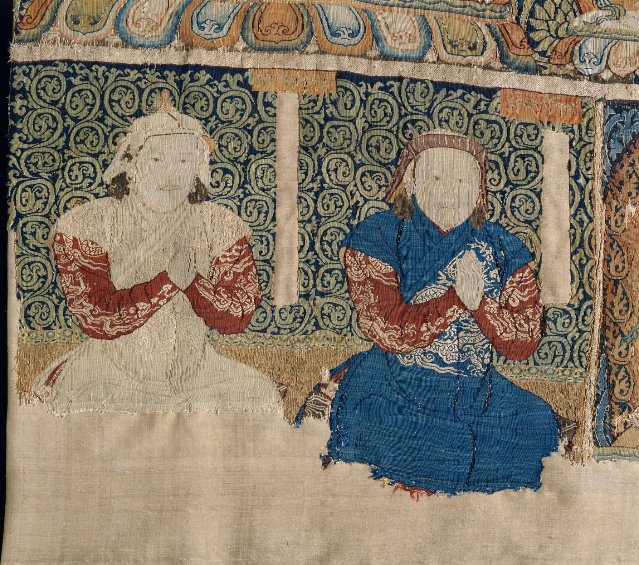 Embroidered textile featuring two robed men kneeling in prayer before green and blue scrollwork background