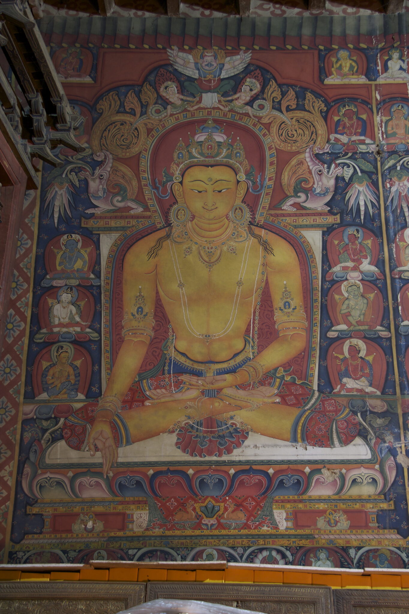 Yellow Buddha seated on lotus throne decorated with fantastical creatures, floral motifs, and scrollwork