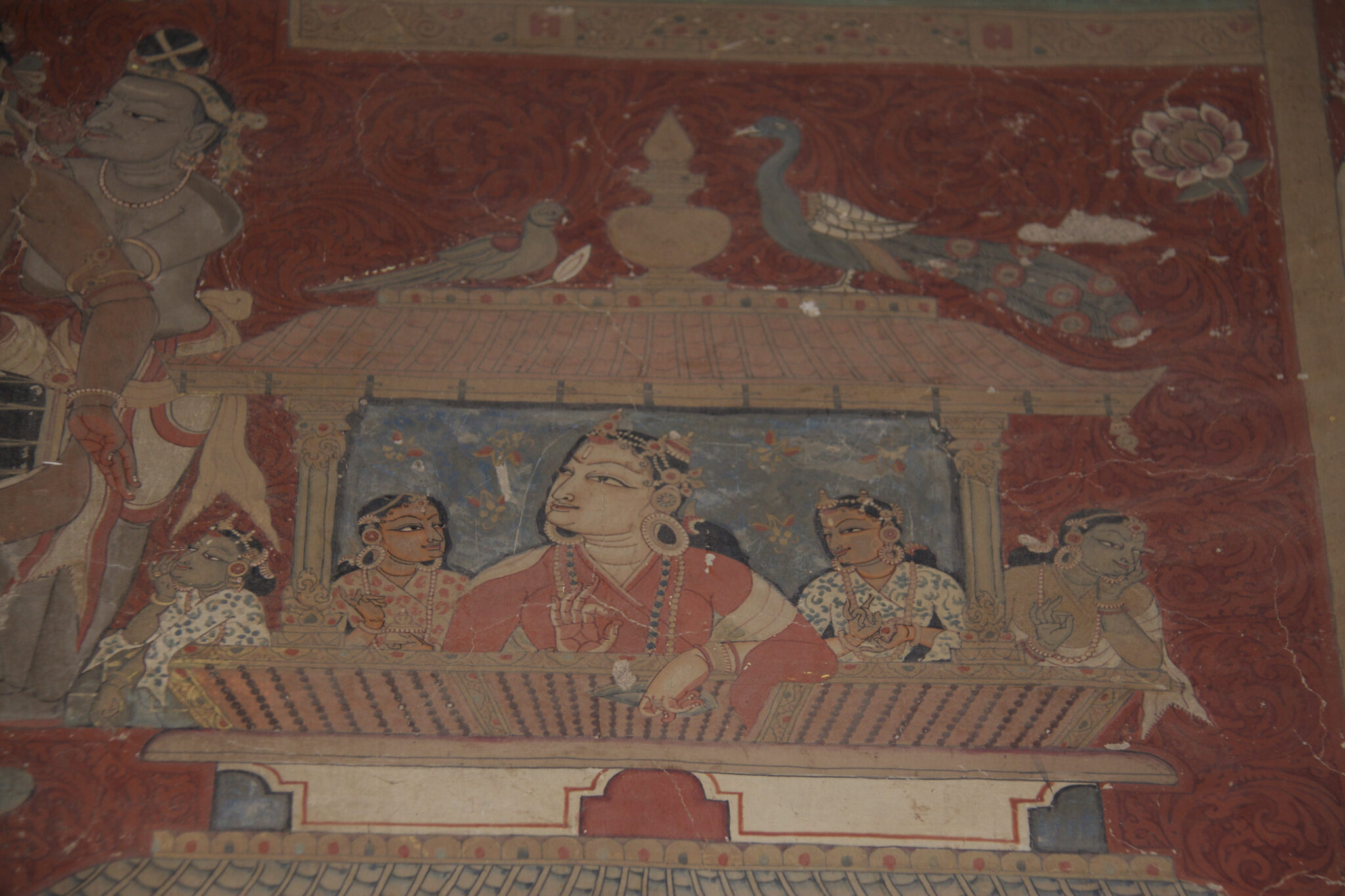 Five elegantly attired women gaze out from balcony of canopied structure while peacocks roost on roof