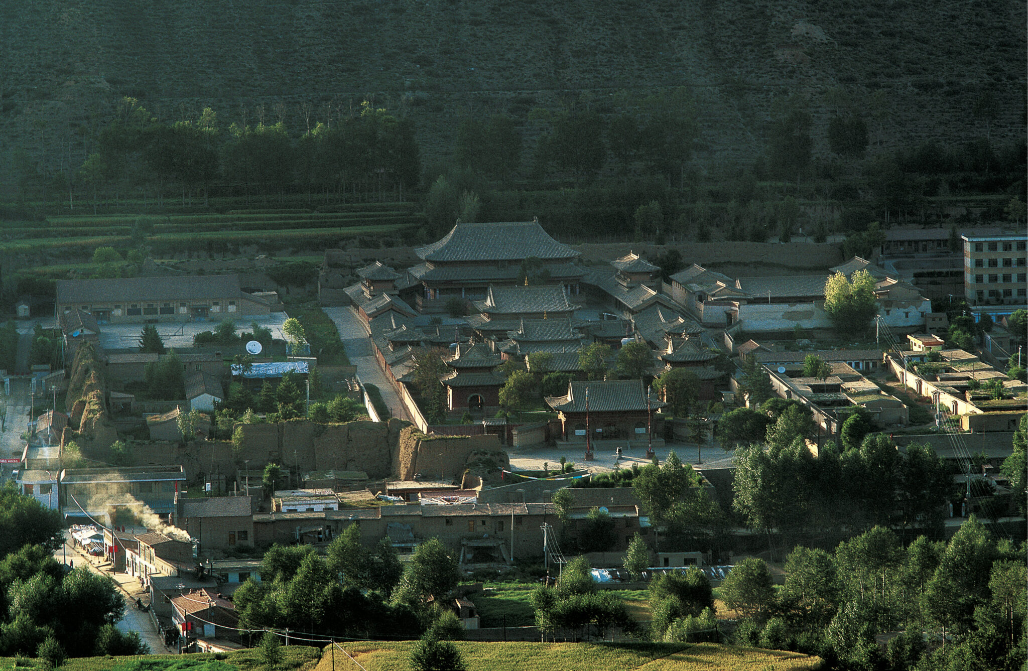 Aerial wide view of building complex in square shape; dozens of constituent structures with sloping, tiled roofs