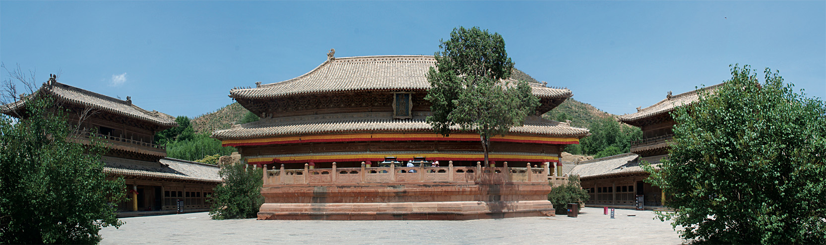 Comprehensive view of courtyard dominated by multi-story building featuring woodwork balustrade and sloping roofline