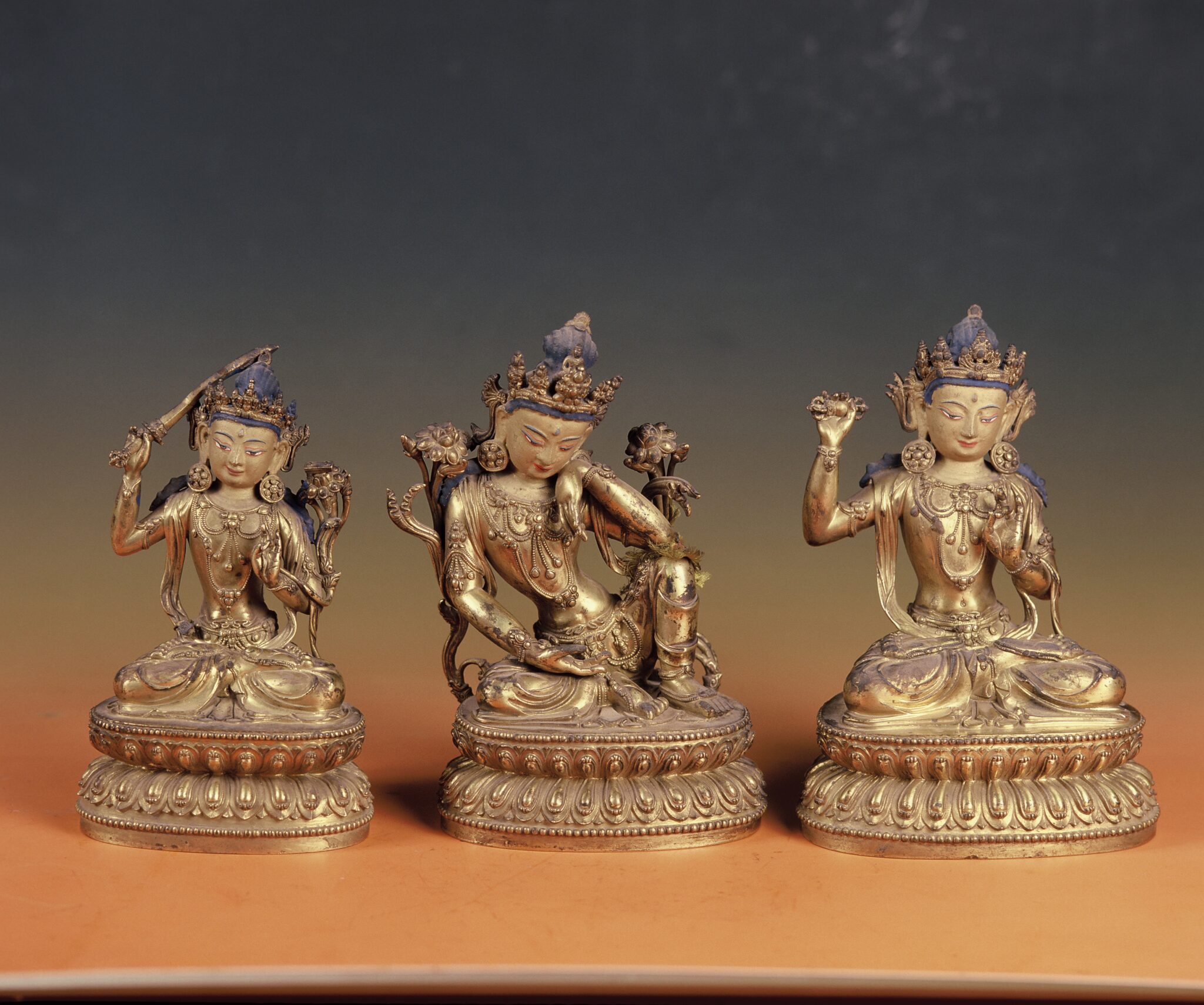 Three gilded Bodhisattva statuettes: one holds sword in left hand, one sits pensively, one holds vajra in left hand