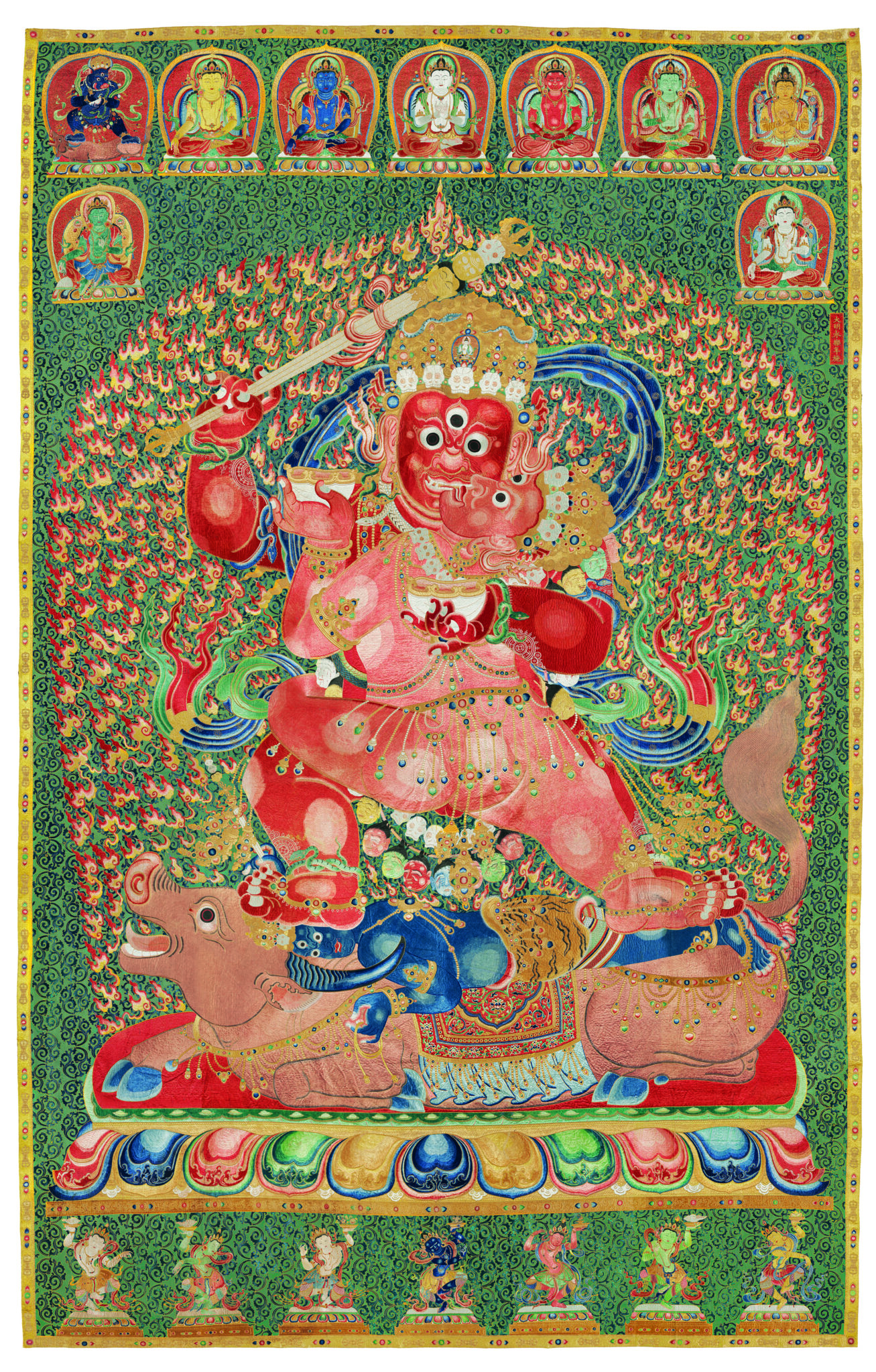 Wrathful red- and pink-skinned deities stand locked in embrace atop prone figure and hooved animal before fiery nimbus