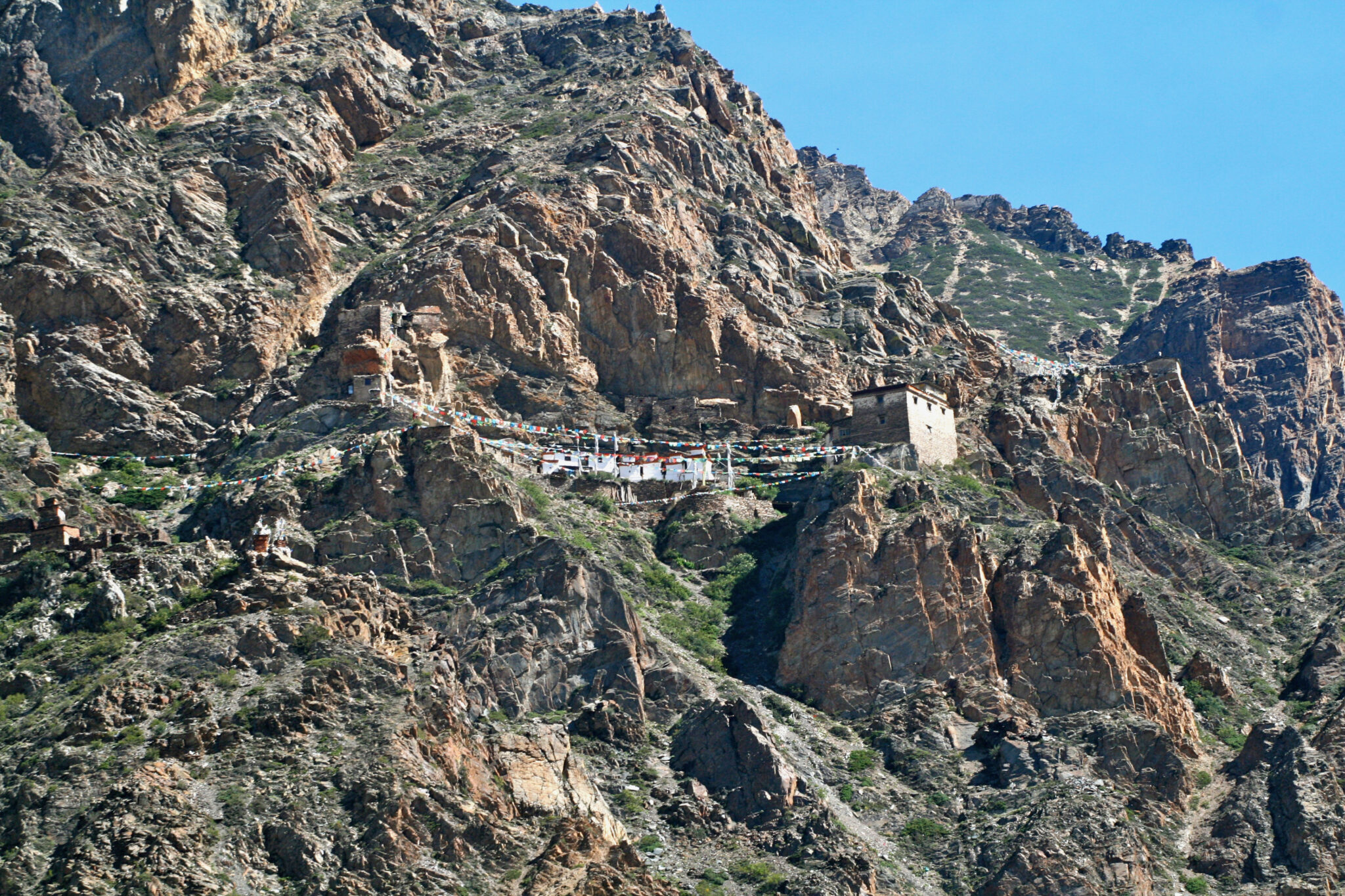 Low-slung building and short tower cling to face of craggy, scrub-covered mountainside