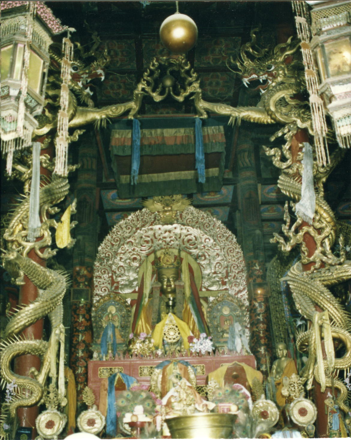 View through columns decorated with coiled dragons of deity statue seated before silver nimbus