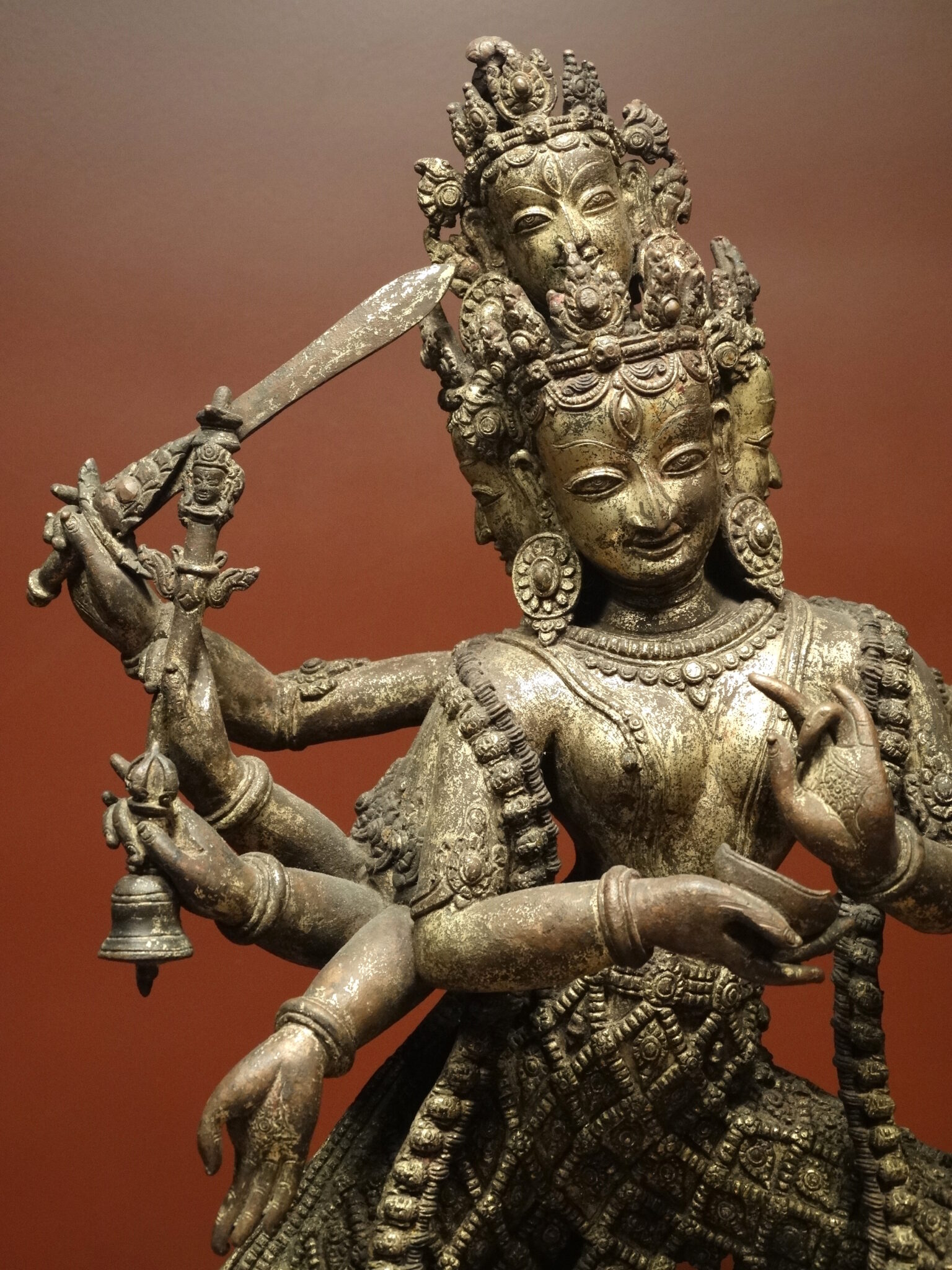 Upper body of bronze-colored statue depicting goddess holding sword and other implements in her many hands