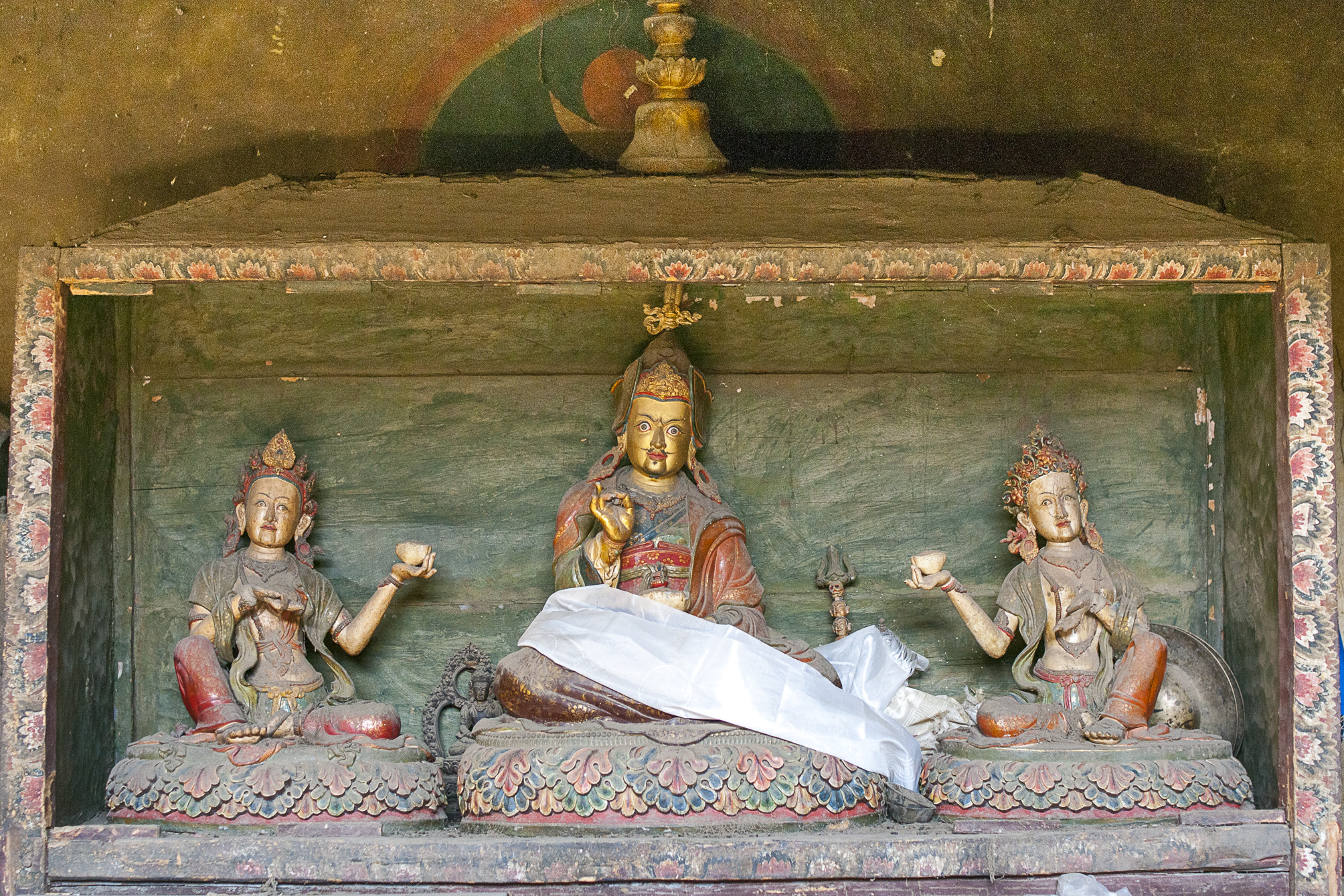 Three sculptures depicting seated figures situated in small green niche; middle figure adorned with prayer scarf