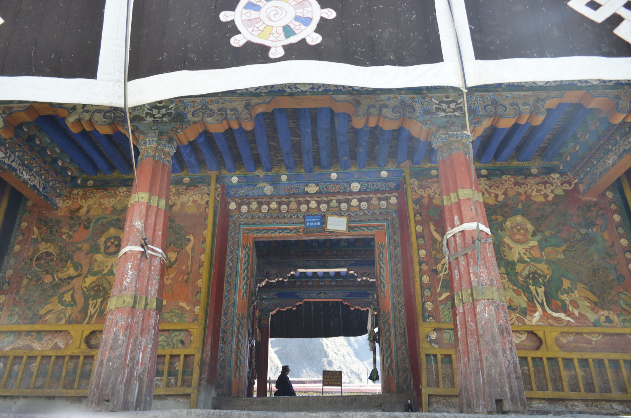 Monumental porch featuring blue timbered ceiling and red columns covering two large murals flanking ornate portal