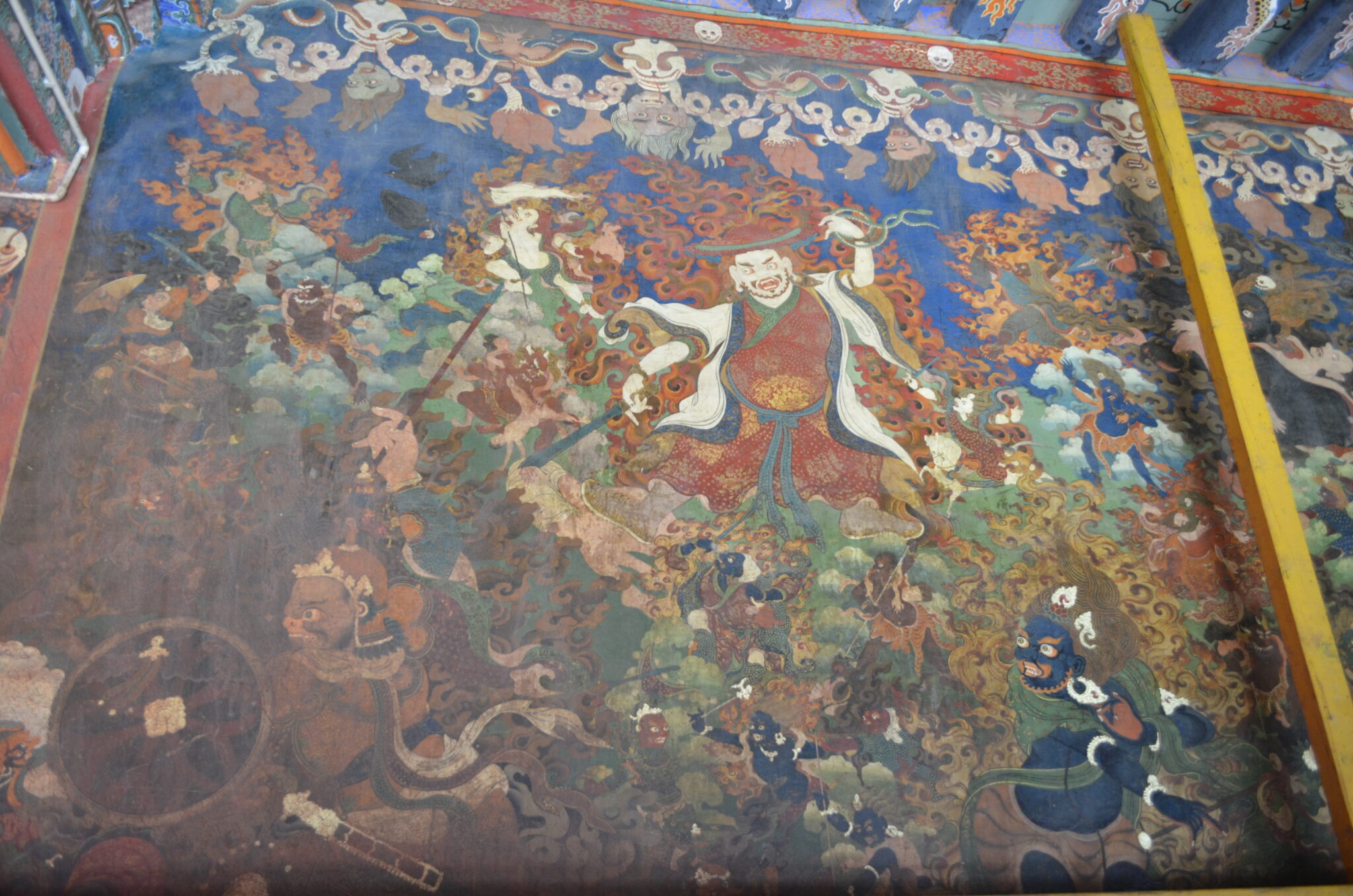 Mural depicting fearsome deity and attendants outlined in flames traveling through green landscape