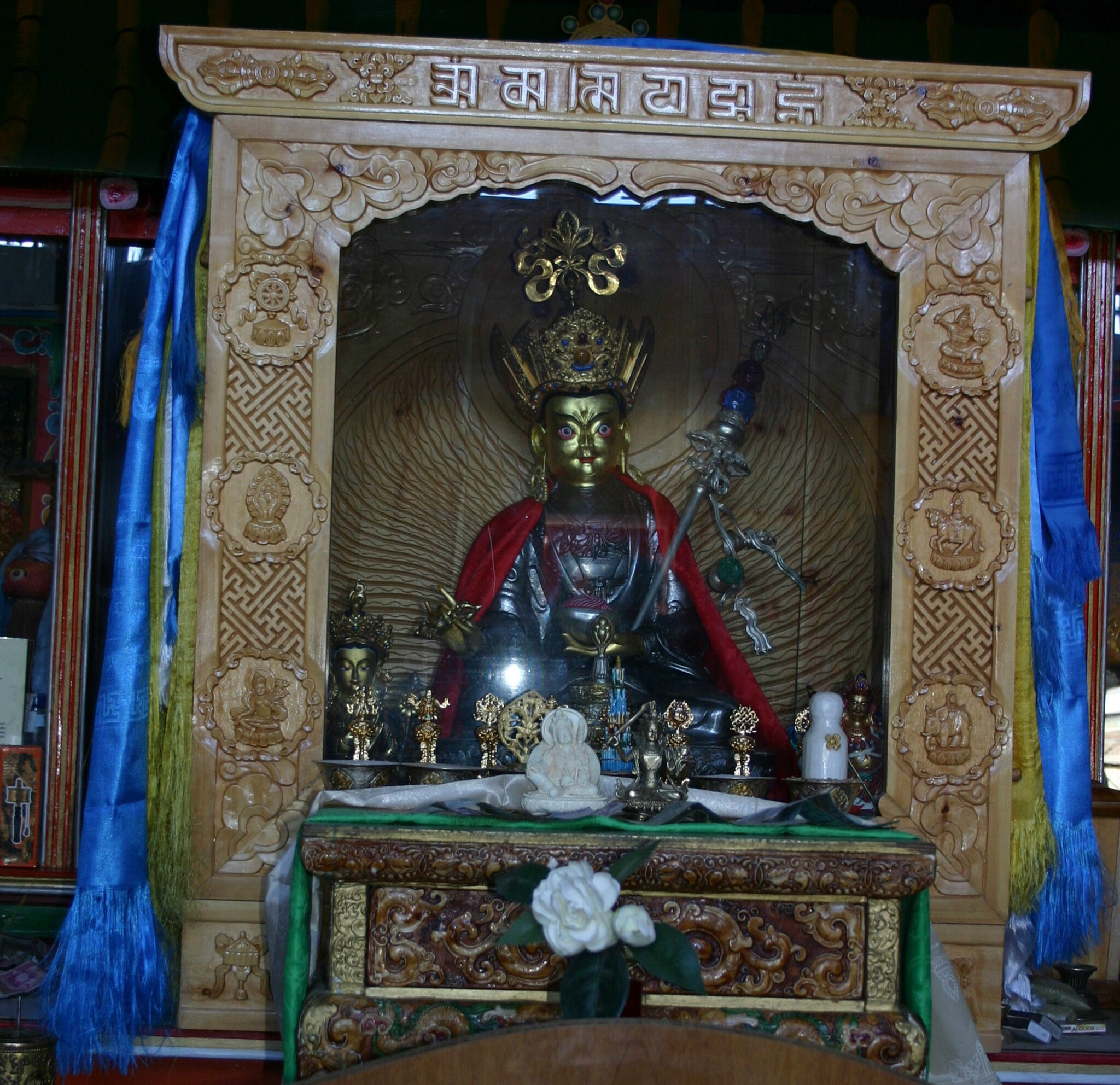 Silver- and gold-colored statue depicting seated Guru; situated in ornately carved wooden cabinet