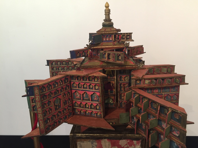 Red-colored religious implement in the form of tiered building with doors opened to reveal dozens of smaller doors opened to reveal portraits