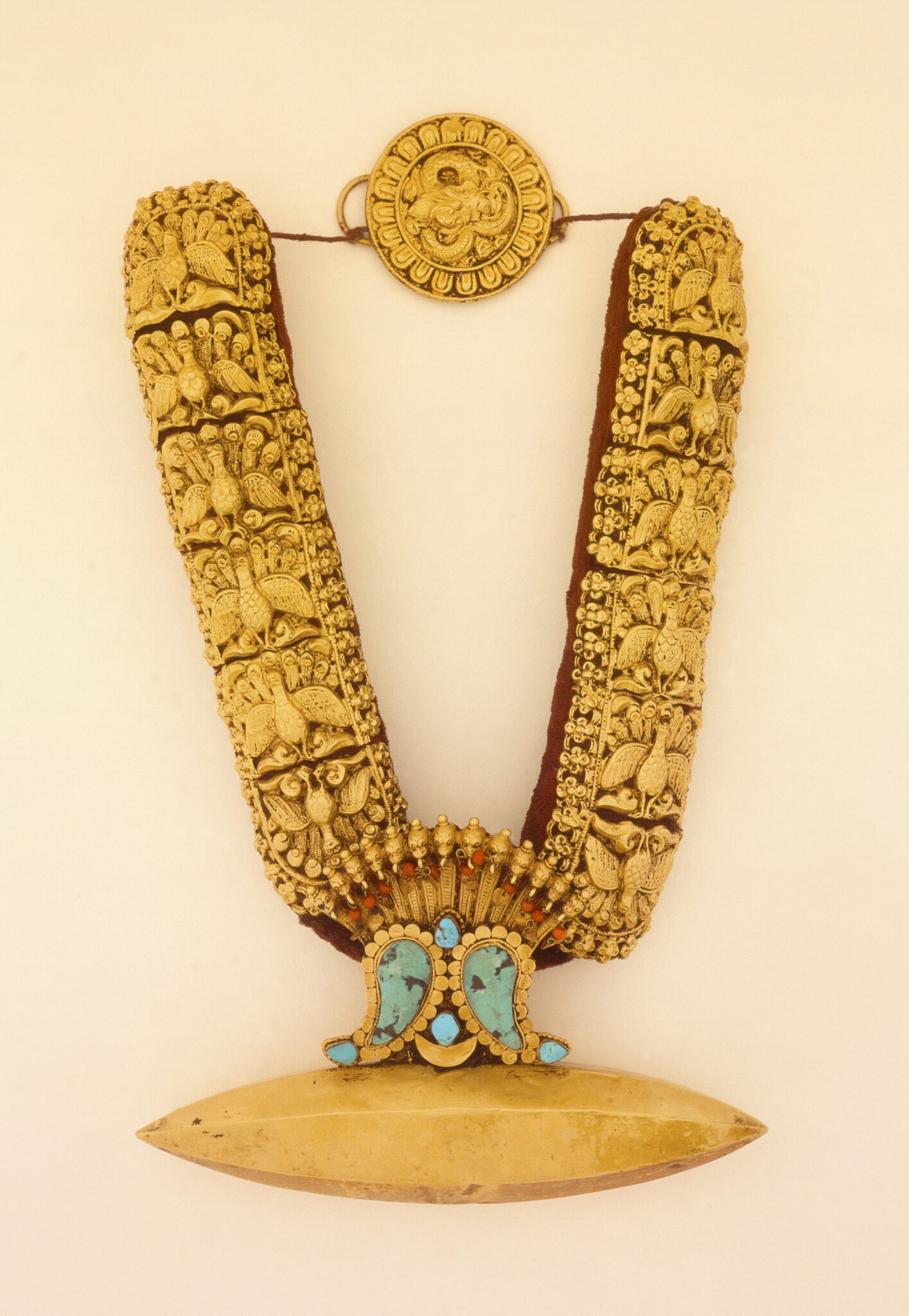 Golden necklace featuring repeated filigree peacock pattern, turquoise insets, and pointed oval pendant