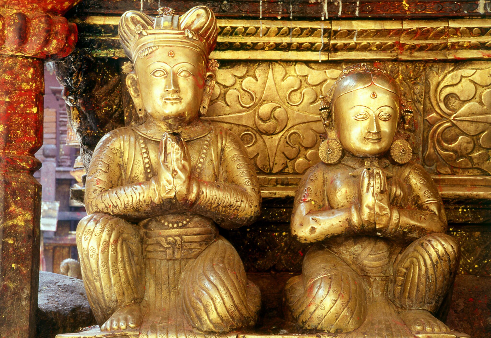 Two gilded sculptures depicting king and female figure kneel with hands in prayer at chests