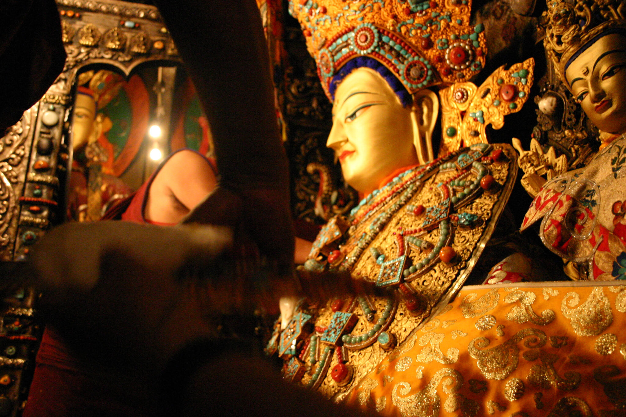 Close, semi-obscured view of magnificently attired golden statue of Buddha being dressed by monks