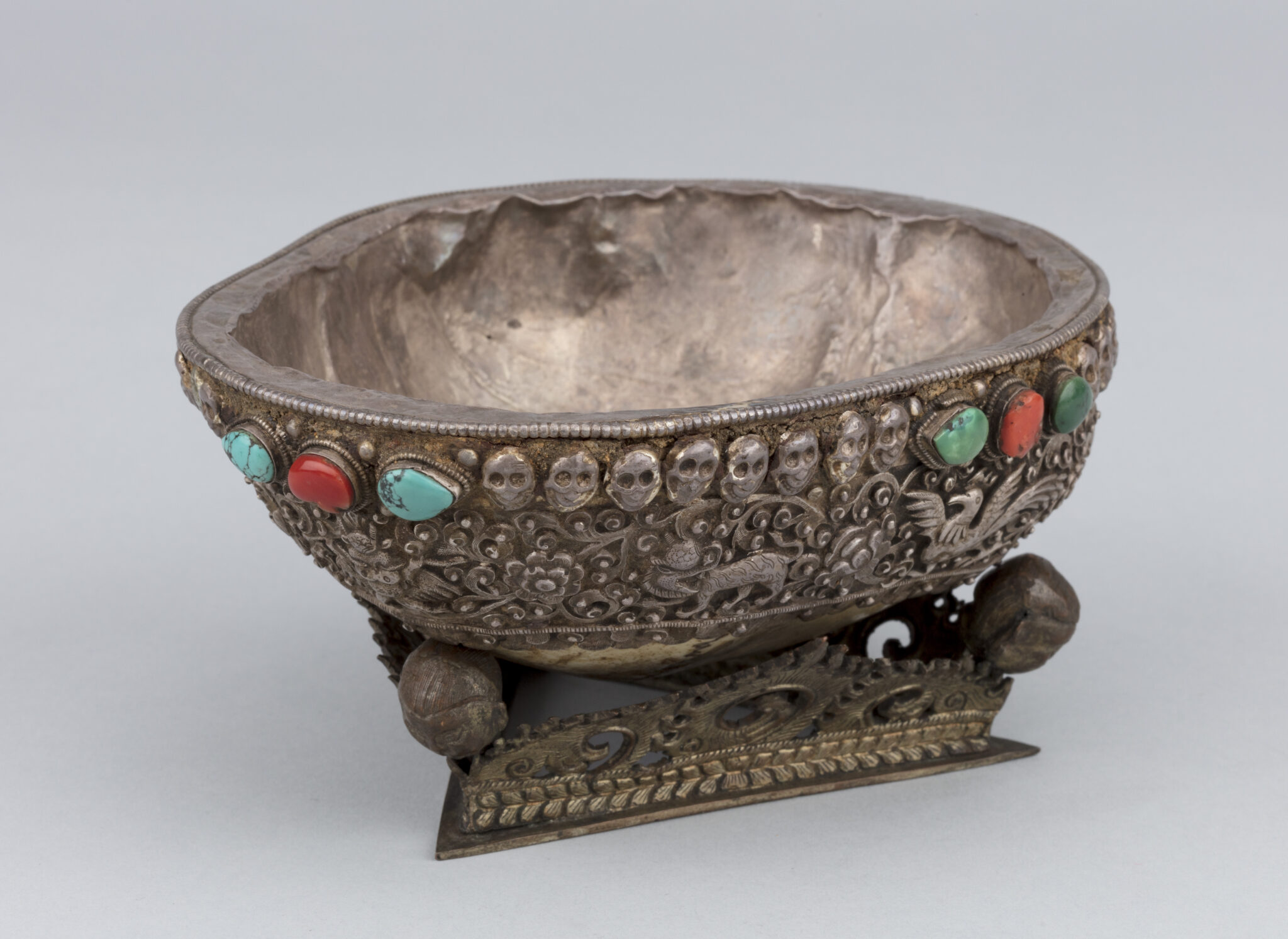 Side view of cup featuring band of silver decoration depicting animals amongst floral motifs and line of skulls