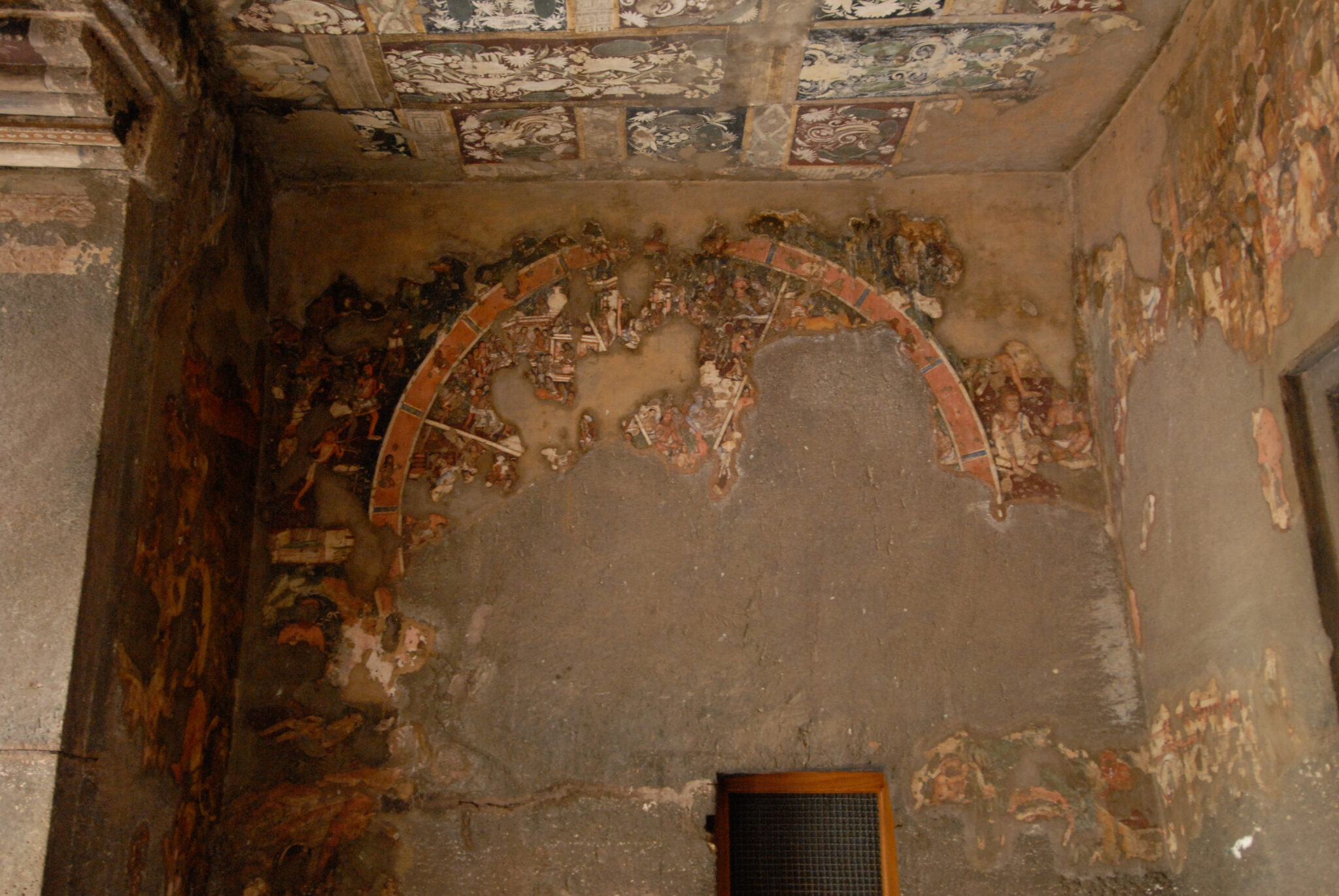 Significantly damaged mural above doorway depicting wheel; sections of wall appear plastered over