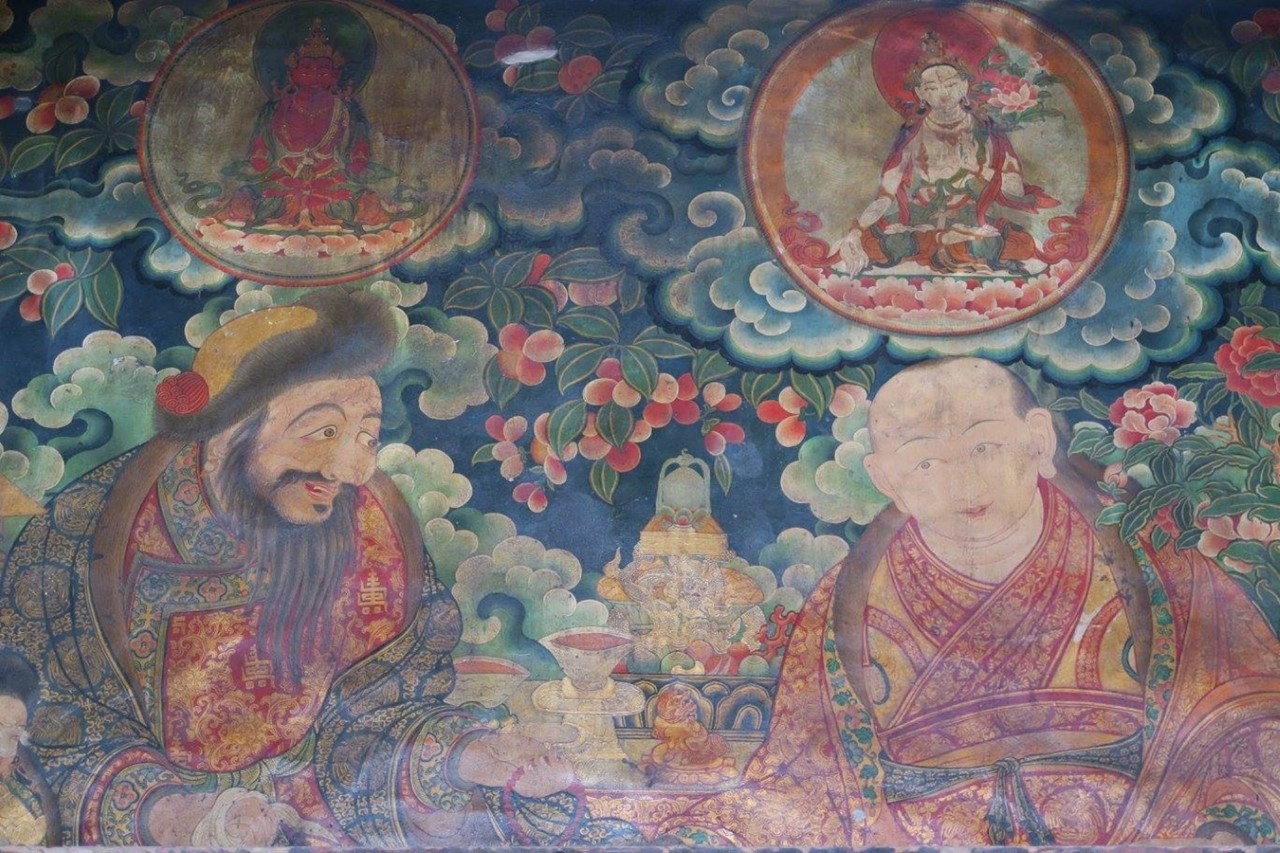 Two splendidly dressed men converse underneath trees, clouds, and roundels featuring seated deities