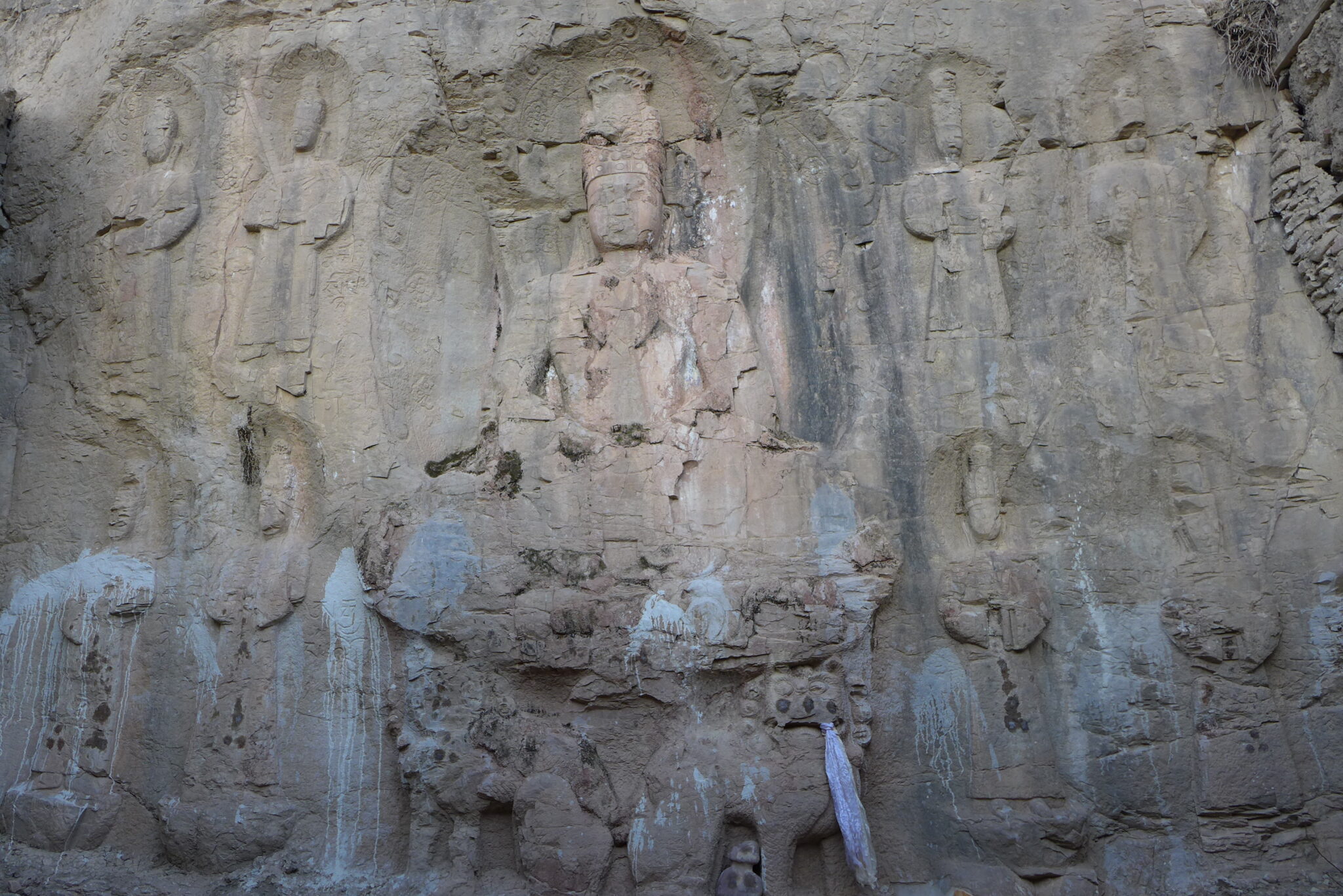 Weathered brown stone relief of Buddha seated on throne and flanked by eight standing Bodhisattvas