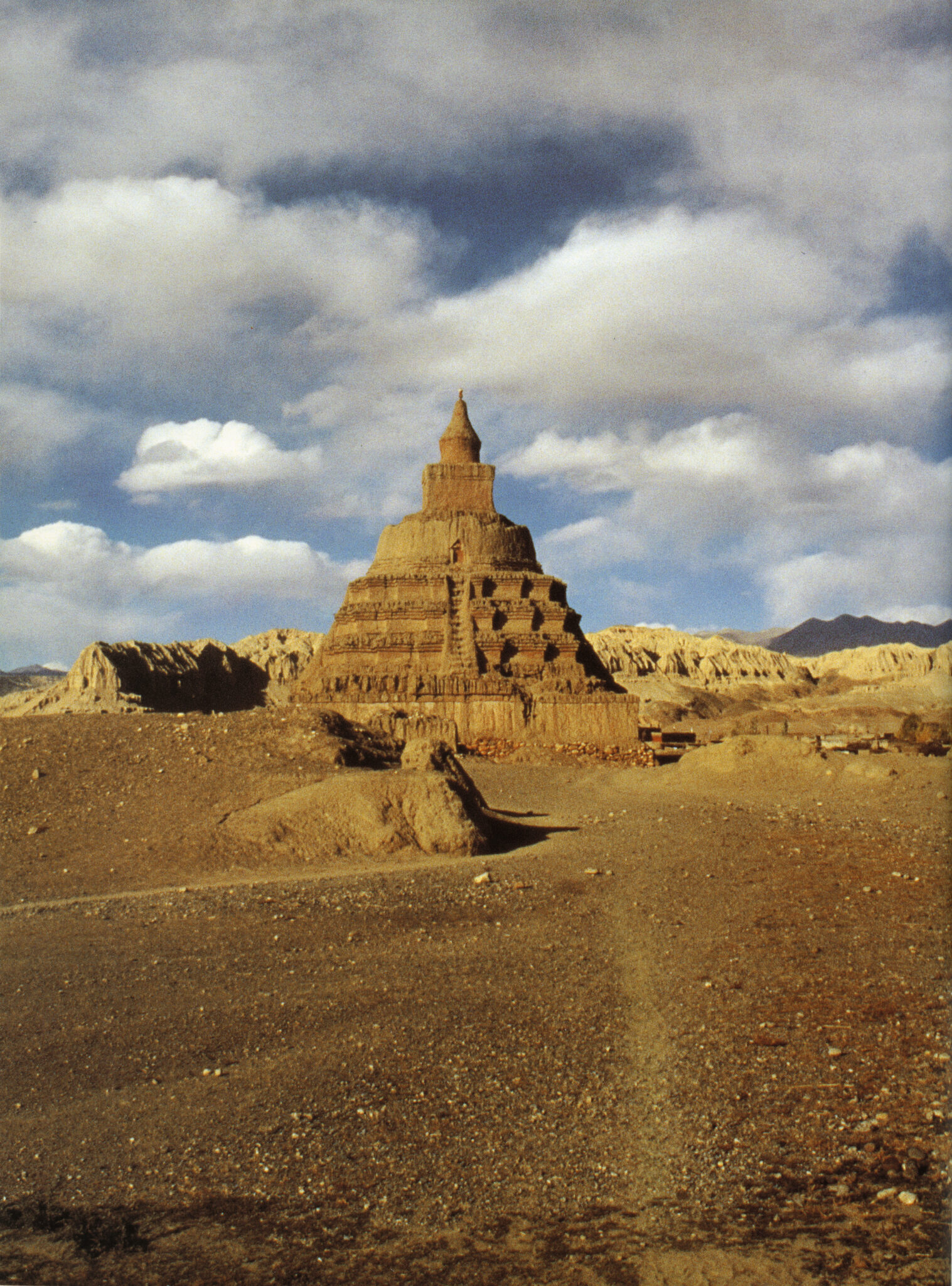 Conical, tiered structure rises into ruddy sky and matches dusky orange-red color of surrounding landscape