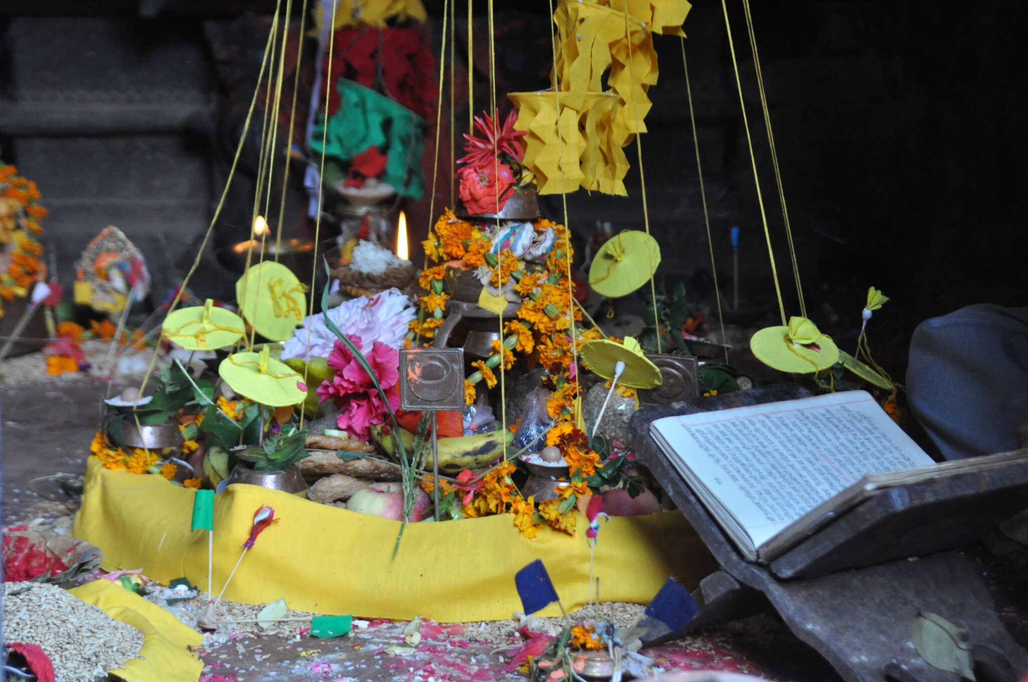 Arrangement of garlands, fruit, ritual implements, and candles contained by band of yellow textile and strings