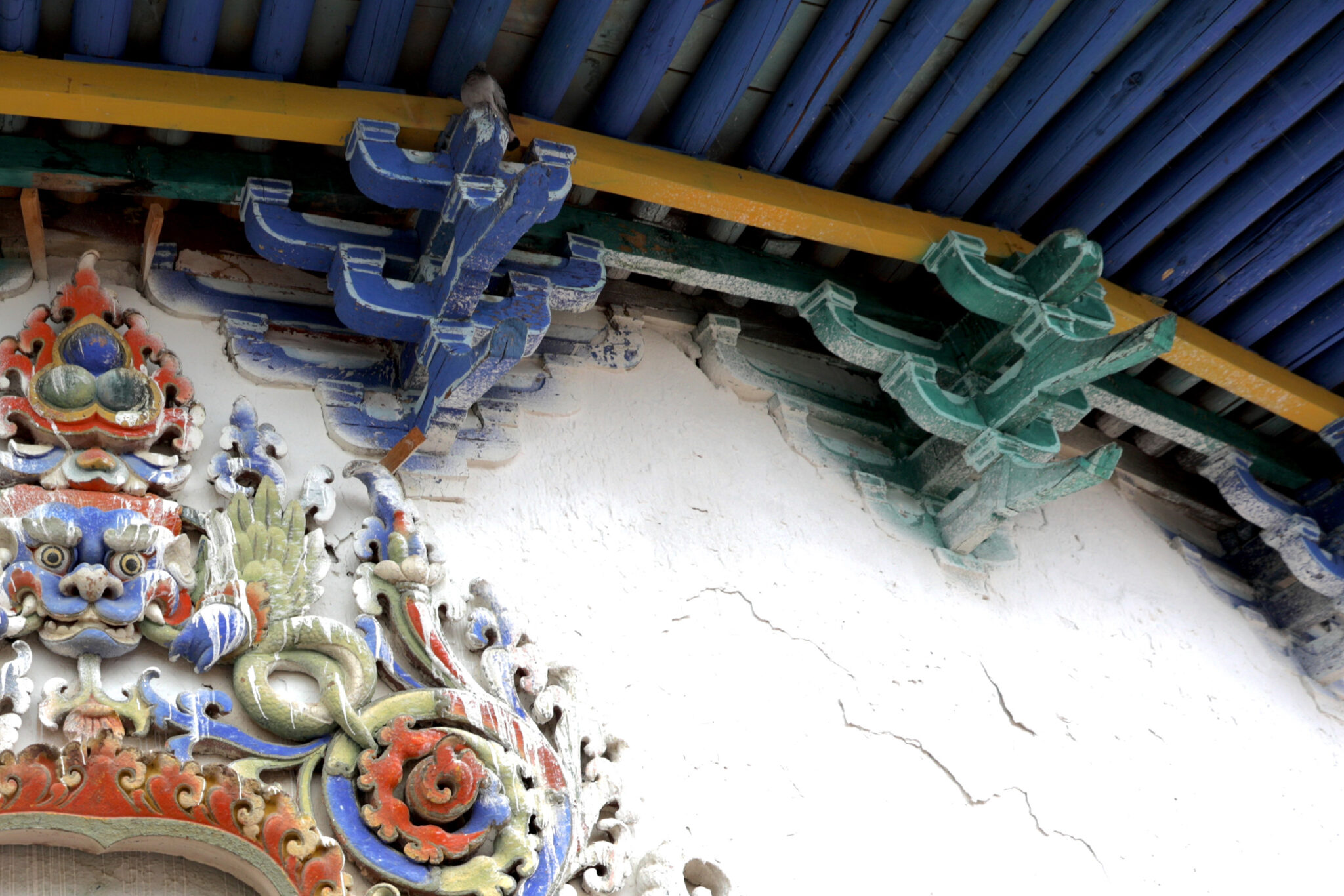 View from below of highly ornamented, brightly painted roof supports above exuberantly decorated pediment