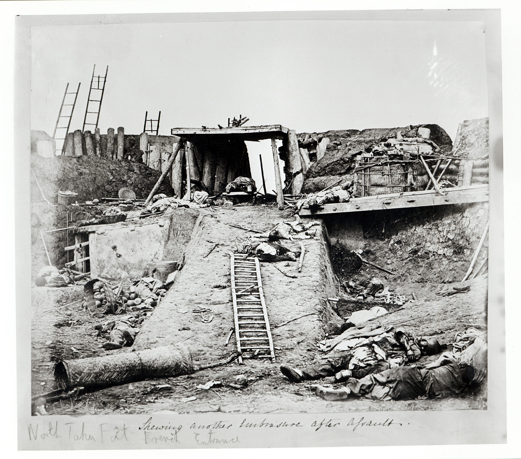 Black and white photograph of destroyed military building with human bodies lying amidst rubble