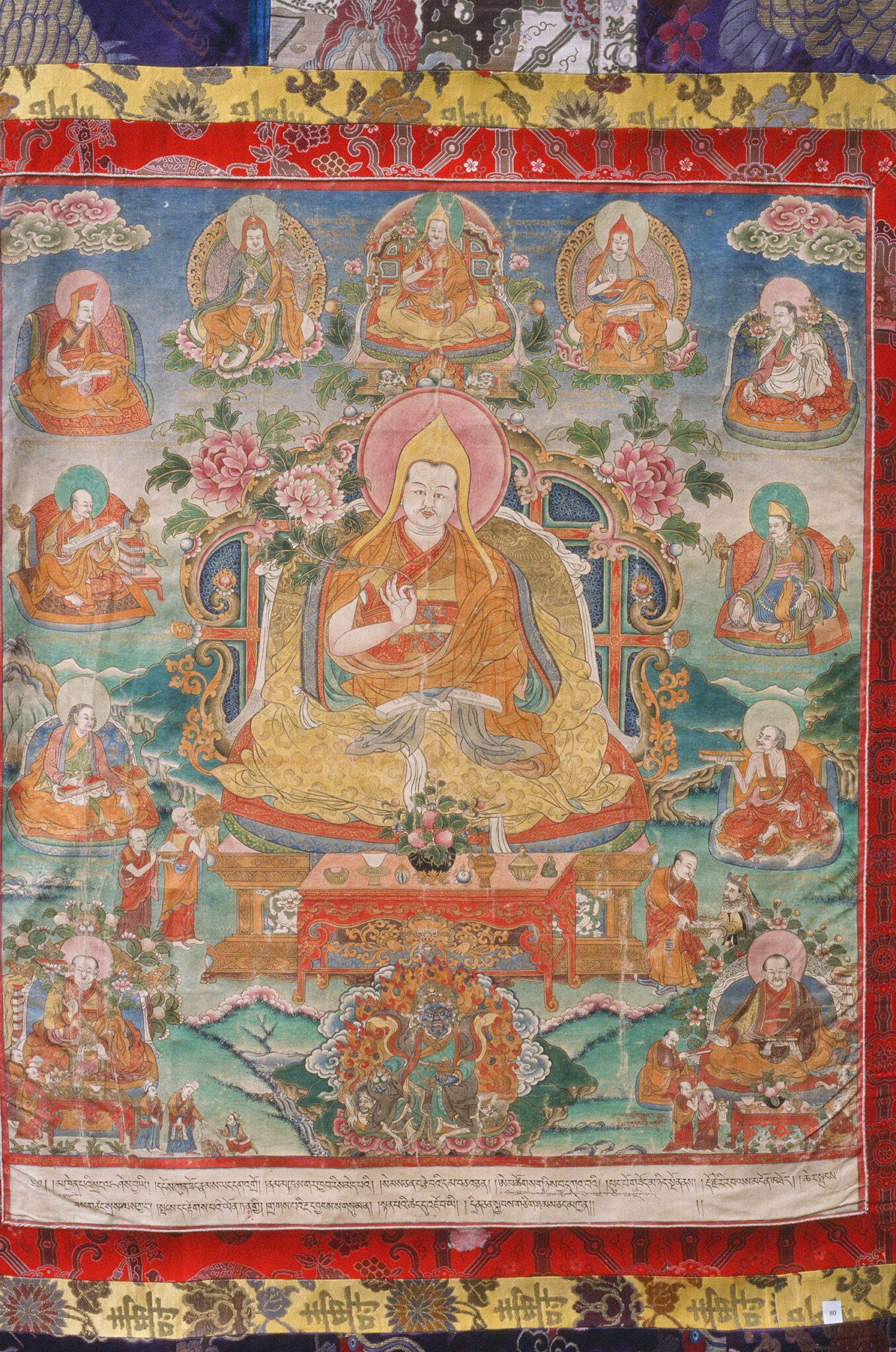 Painting mounted on brocade border depicting seated figure surrounded by small portraits against mountain landscape