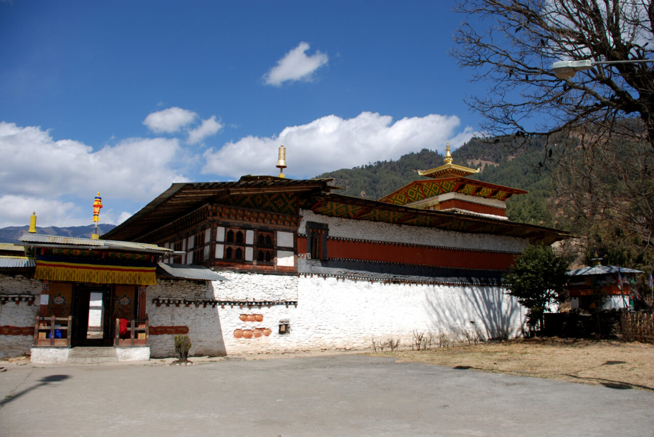 Exterior view of whitewashed temple featuring irregular roofline, ornamented eaves and brackets, and golden pagoda tower