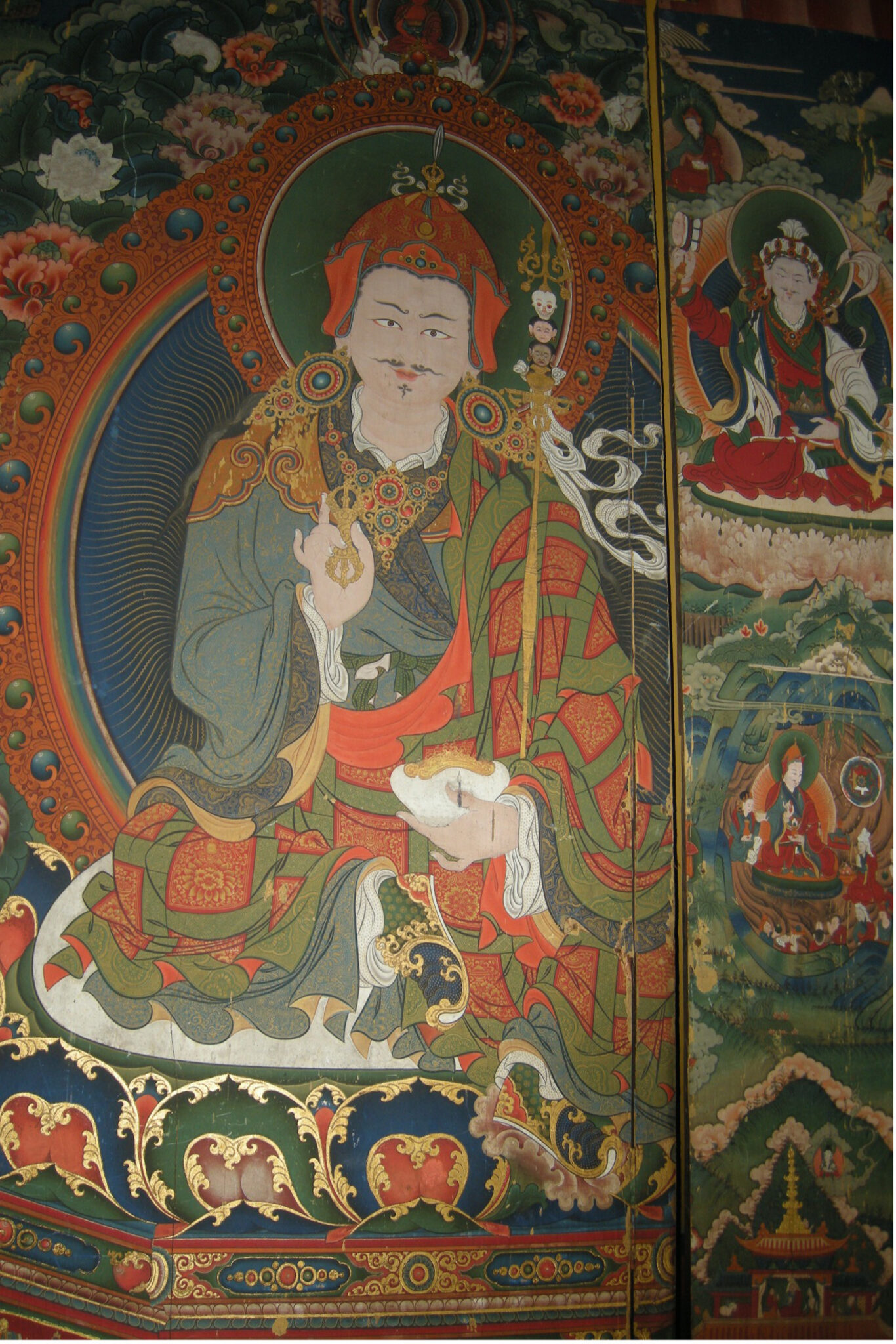 Guru wearing orange and green patchwork robe, holding vajra in left hand at chest