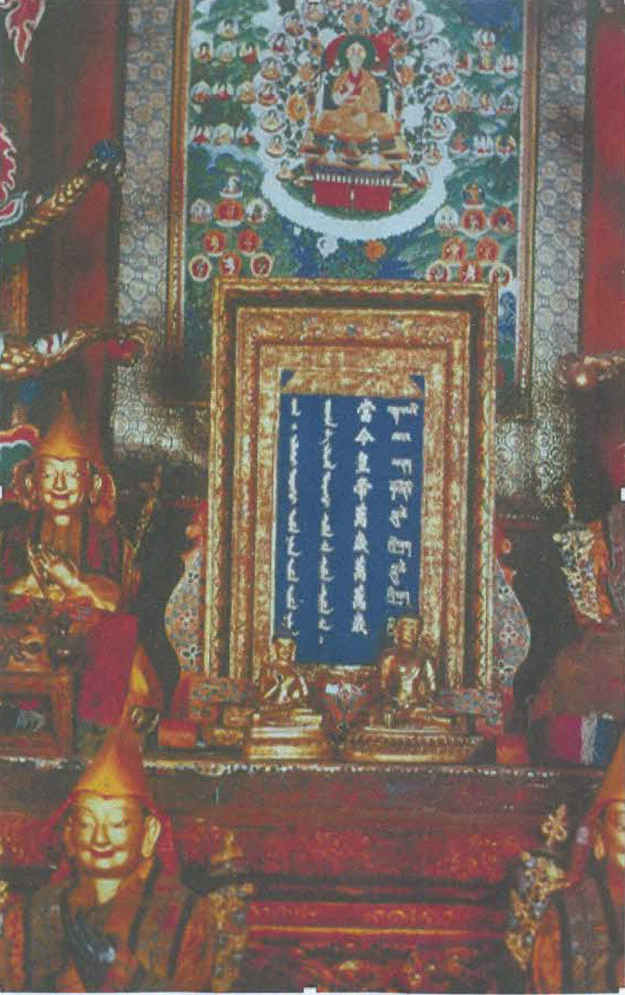 Four lines of text inscribed in gold on blue background, enclosed in gold frame, positioned underneath thangka