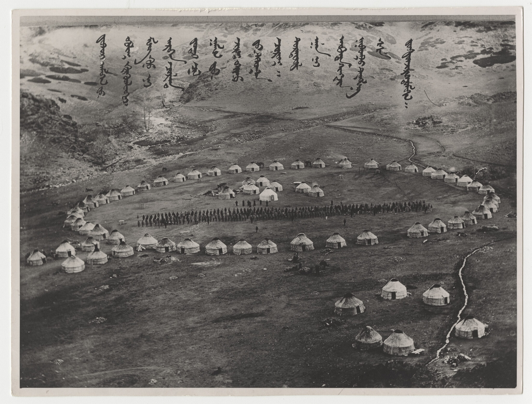 Black and white aerial photograph of domed tents situated in ring formation; text at top