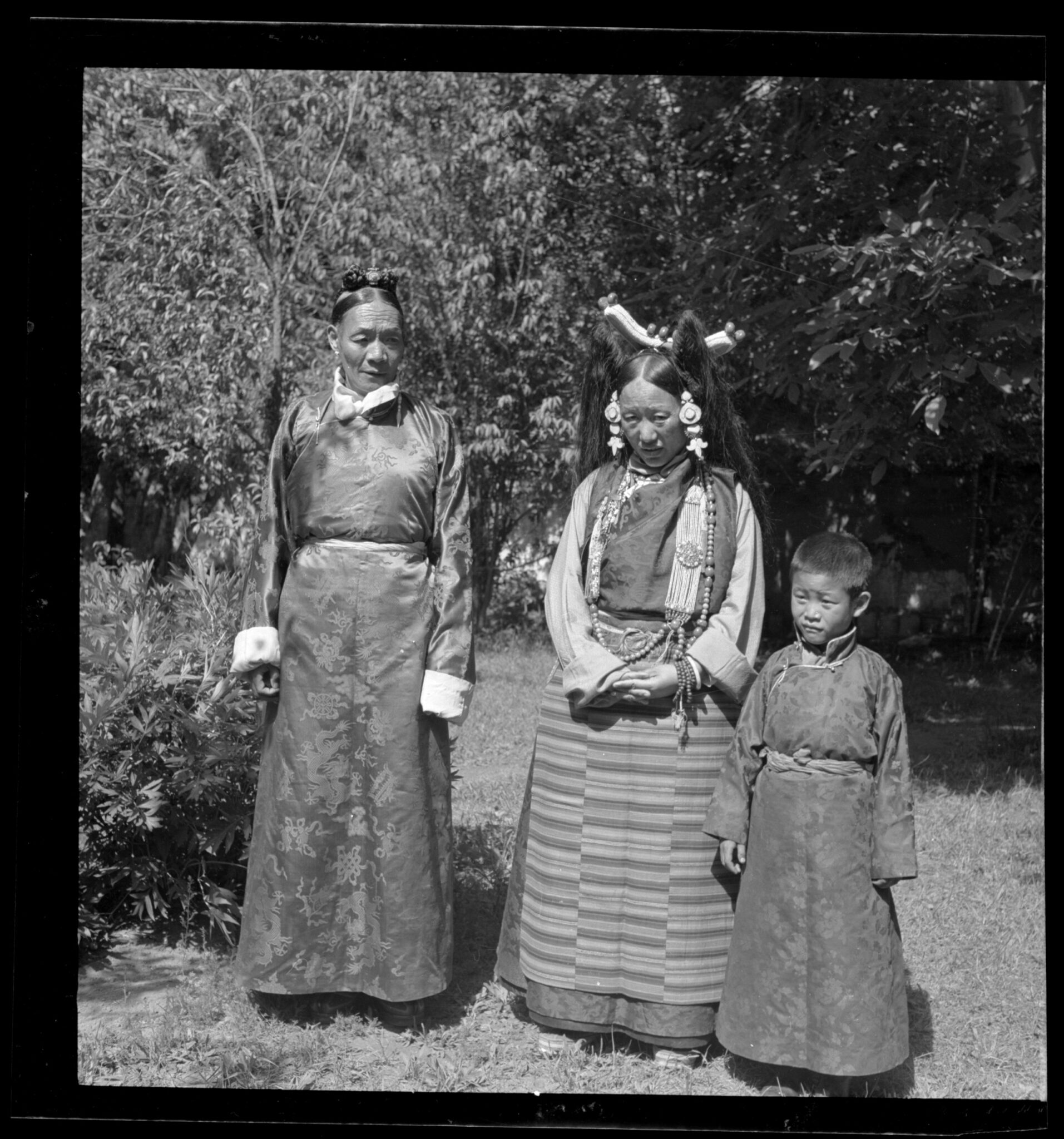 Mother, father, and son, all dressed in sumptuous brocades, pose for photograph in grove of trees