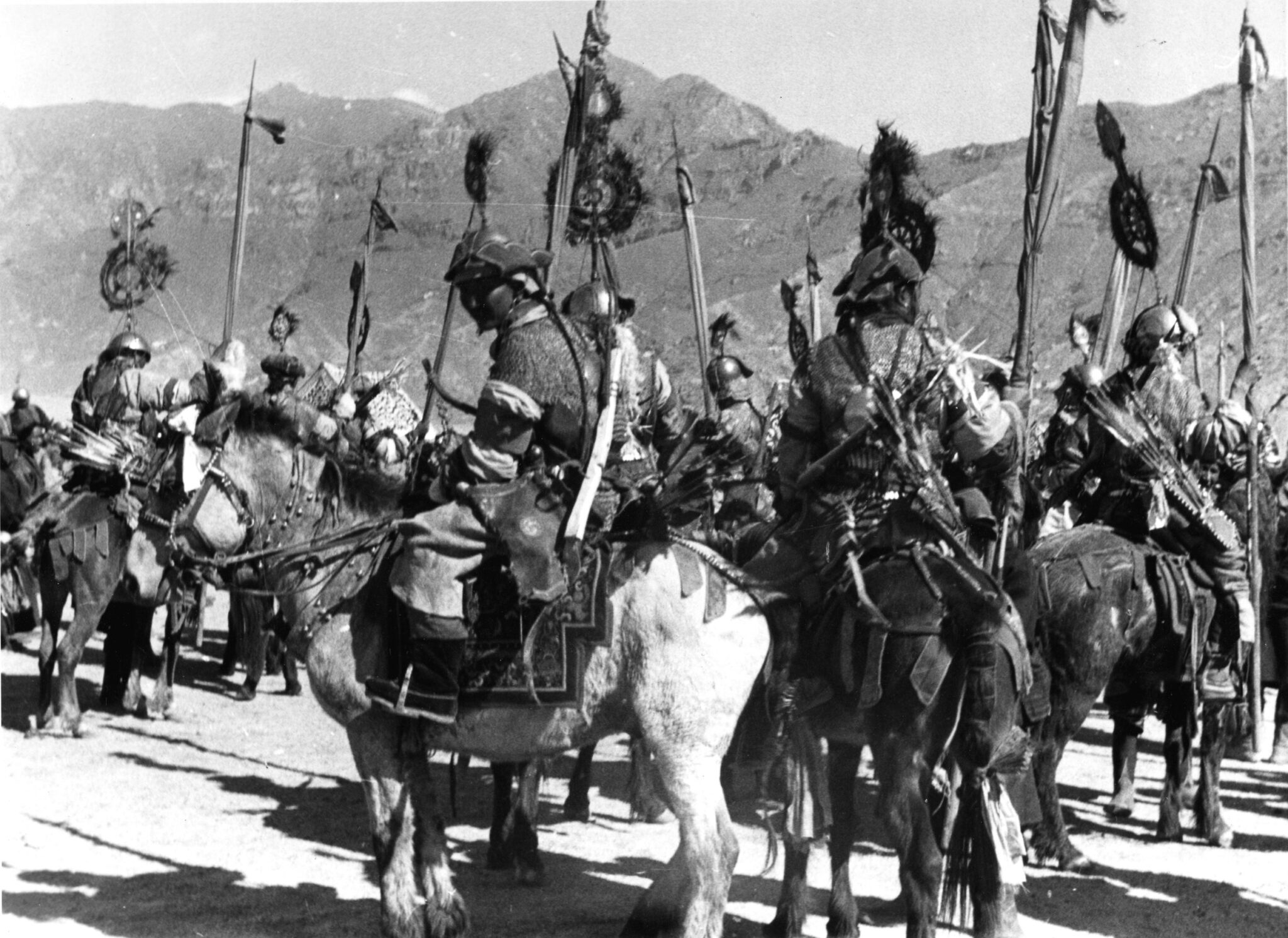 Armored men mounted on horseback, carrying spears and standards, assemble at base of mountain range