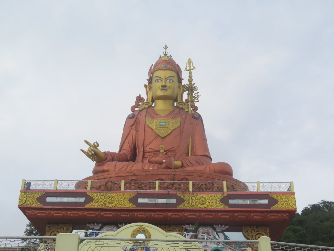 Monumental statue depicting figure in saffron robe seated on pedestal featuring two animals and golden decoration