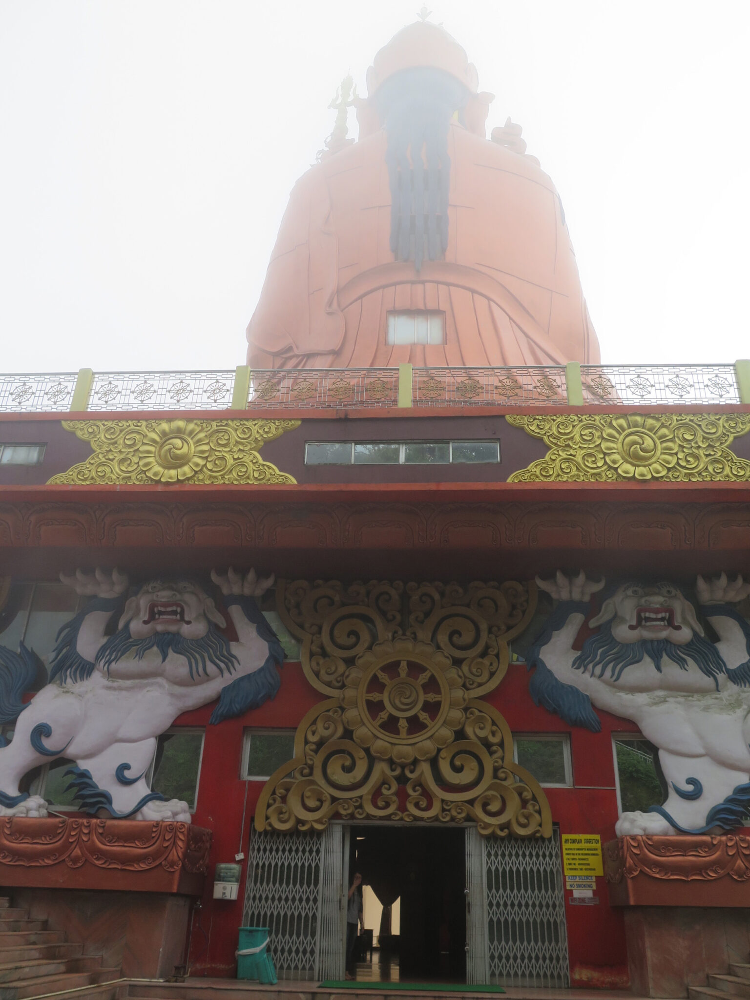 View of door, decorated with fantastical animals, leading to interior of plinth supporting mist-shrouded colossus