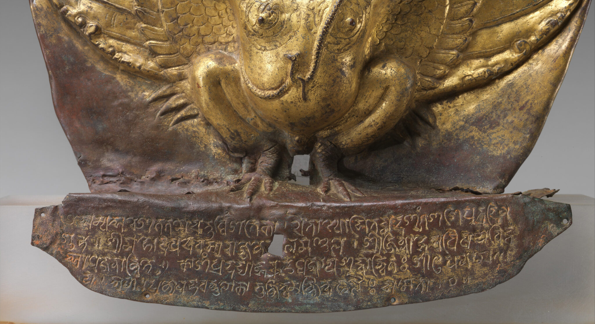 Four lines of Sanskrit inscribed in gold pigment on purple-brown base of relief statue